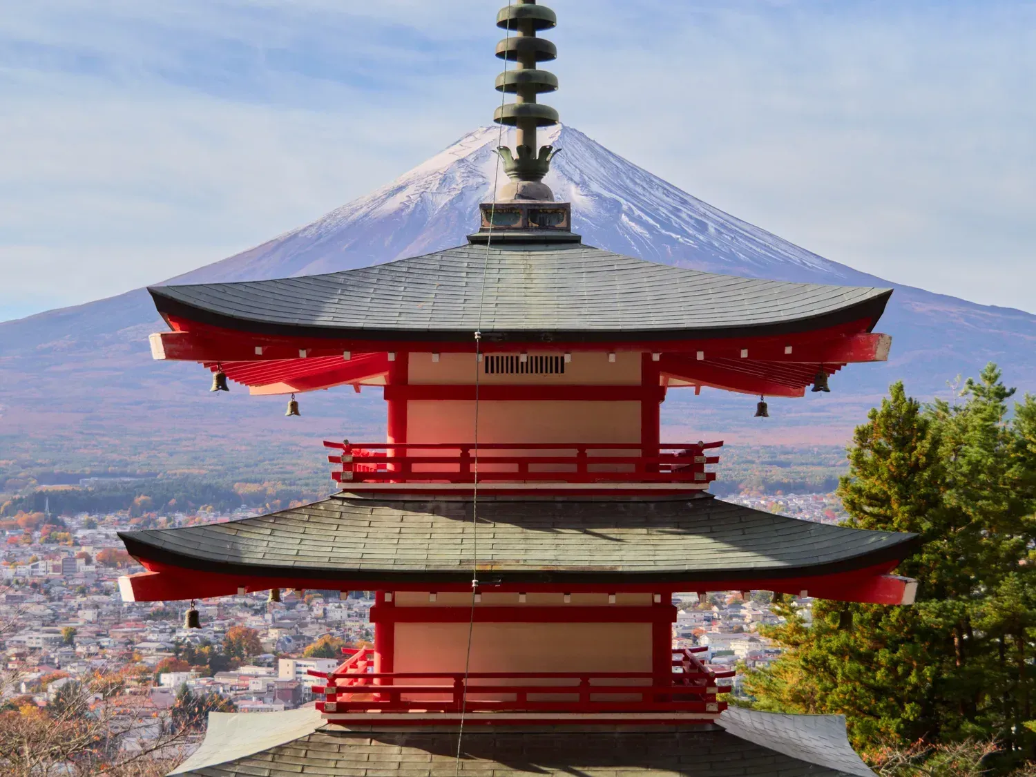 The vermilion five-storey Chureito Pagoda with snow-capped Mount Fuji behind it and the town of Fujiyoshida below
