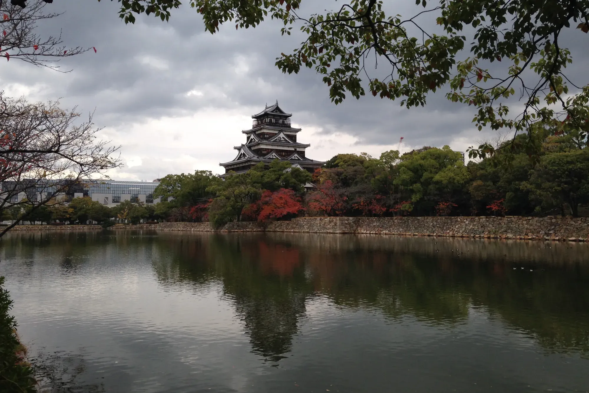 The keep of Hiroshima Castle above autumn trees, reflected in the still water of the moat