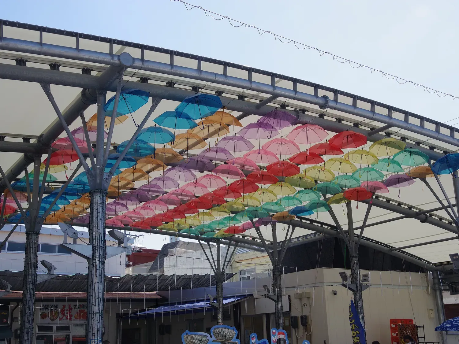 Rows of open umbrellas in pastel colours hanging under a steel canopy at Itoman Market Itomaru