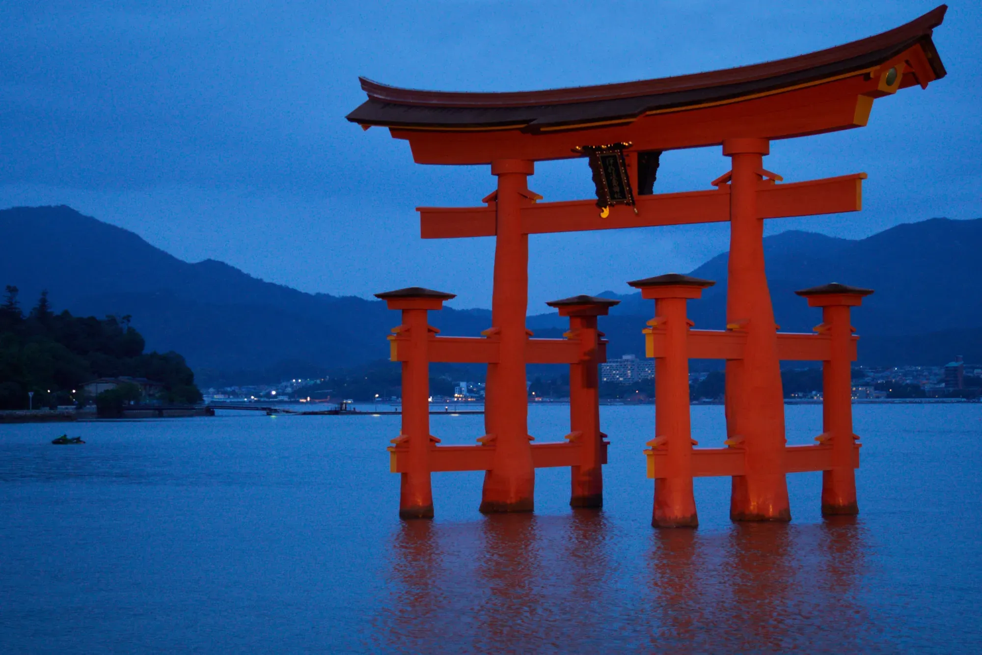 The great torii of Itsukushima Shrine standing in the sea at high tide, with mountains behind