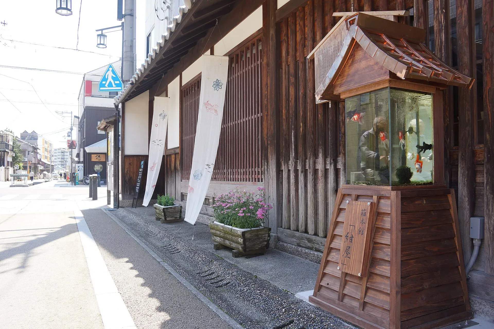 A lantern-shaped goldfish tank standing in front of an old wooden townhouse on a street in Yamatokoriyama