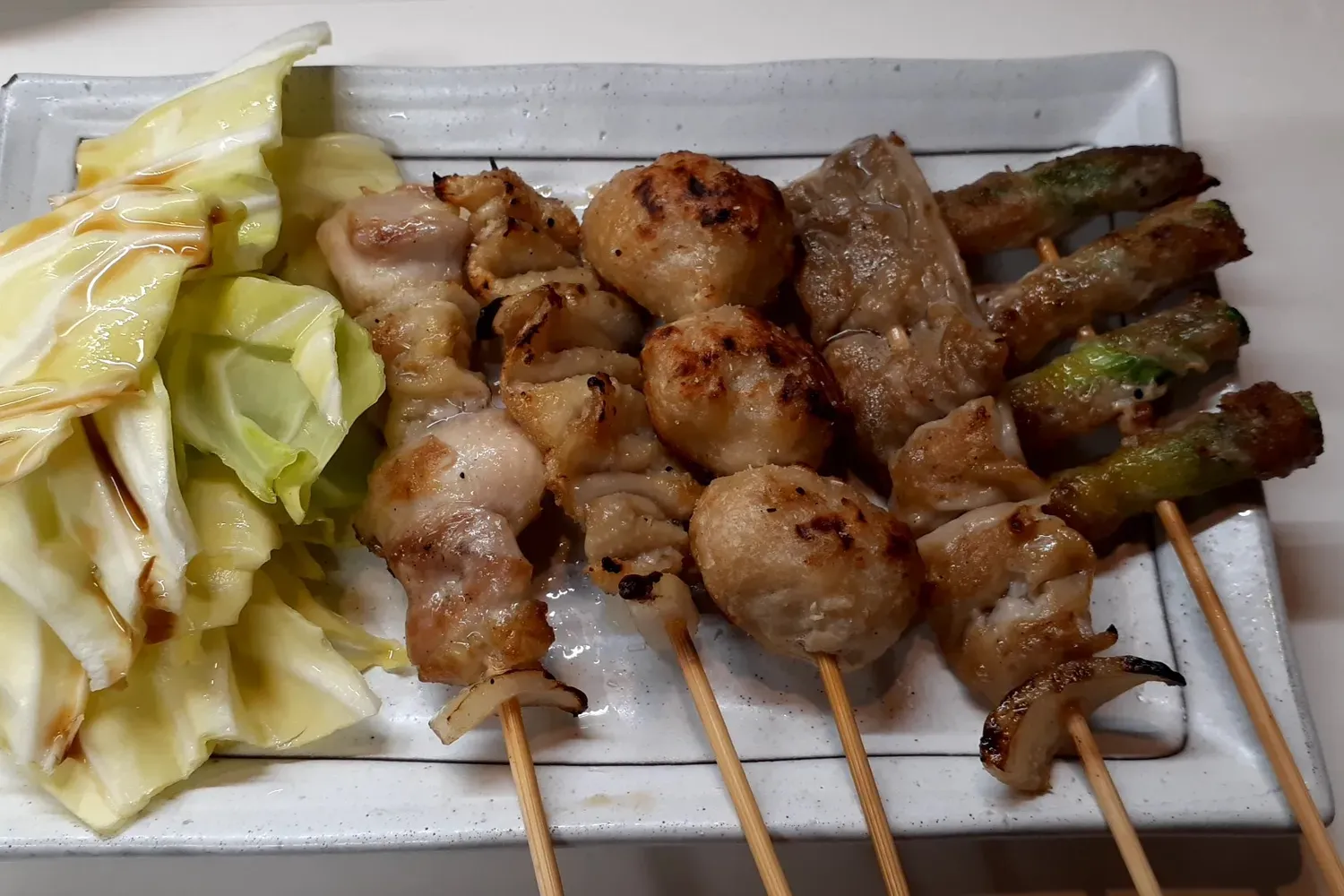 Grilled yakitori skewers on a white plate beside a heap of raw cabbage leaves