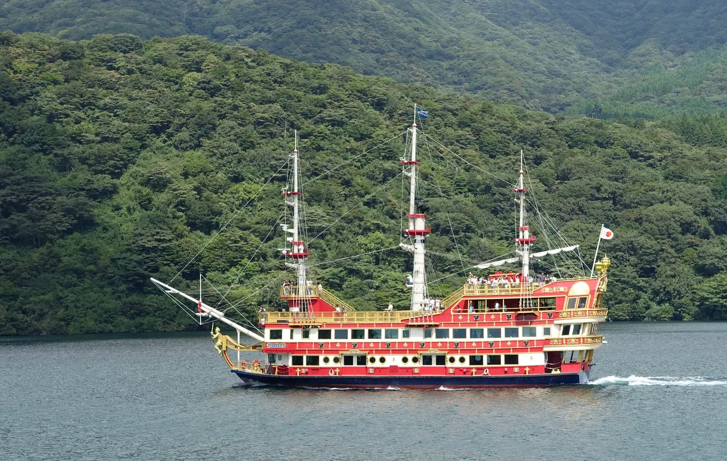 A replica sailing warship with red and gold decoration crossing Lake Ashi below green forested hills