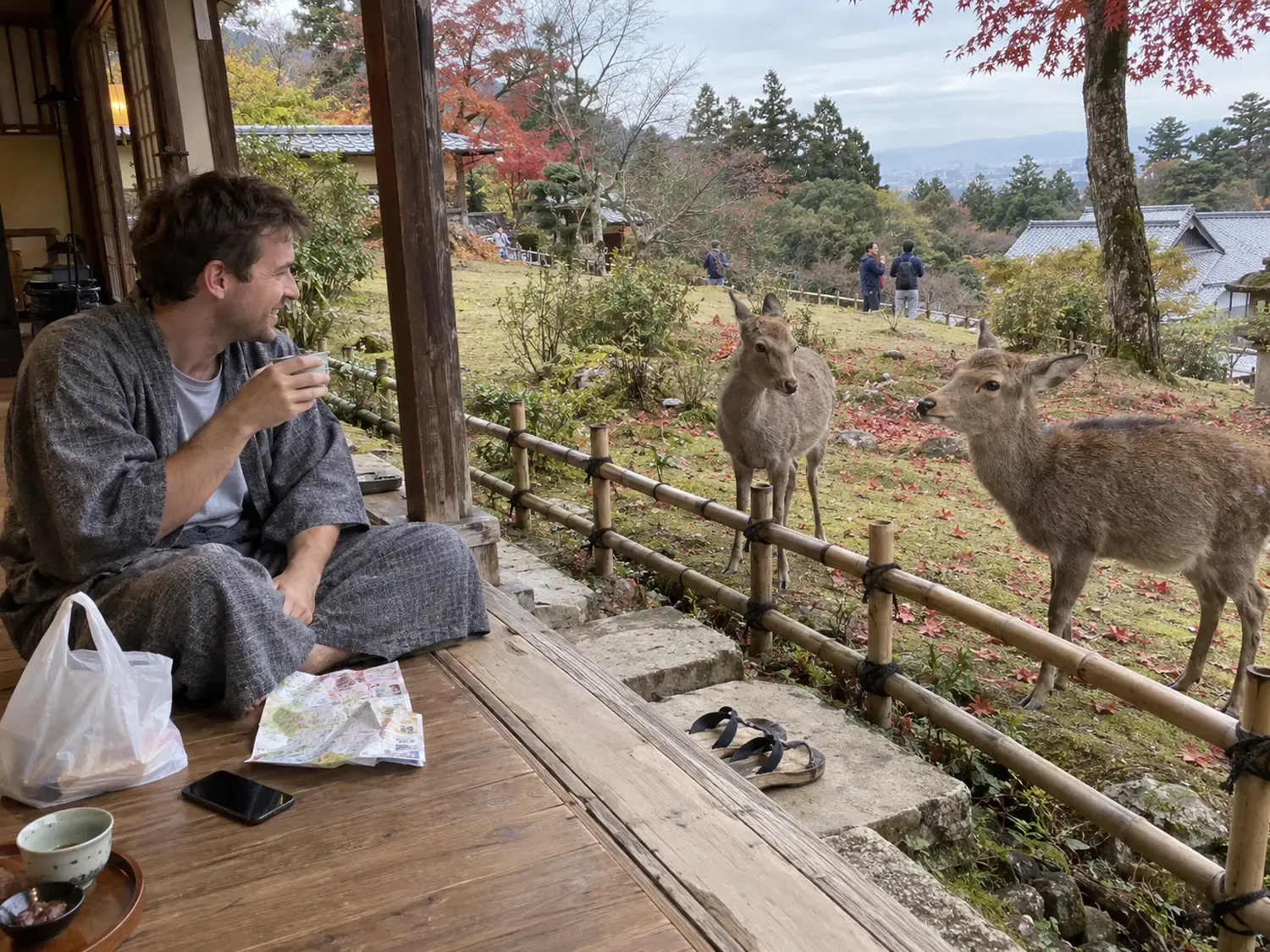 A traveler in a yukata sitting on the wooden veranda of an inn with a cup of tea on an overcast autumn afternoon, smiling at two deer standing just beyond the low bamboo fence