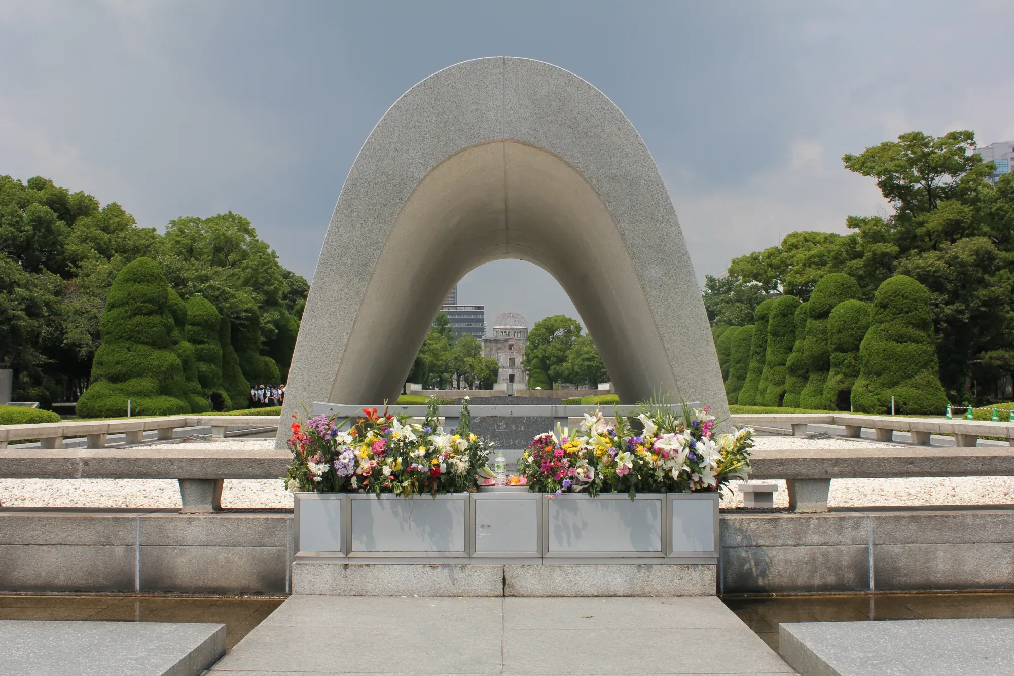 The arched Cenotaph for the A-bomb Victims with flowers in front, and the A-Bomb Dome visible in the distance through the arch