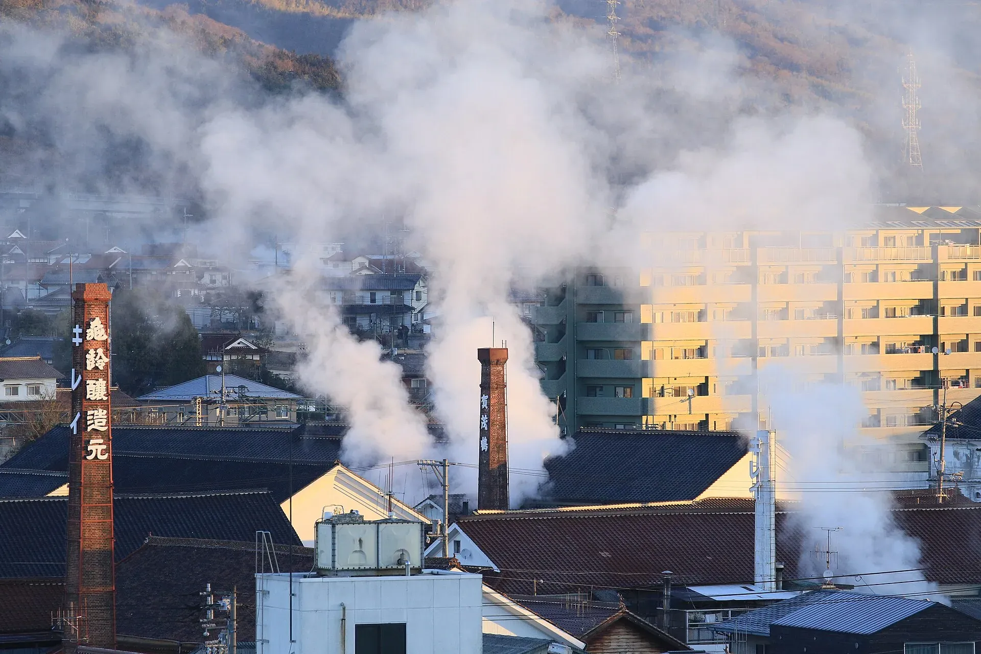 Steam rising from brewery chimneys, one of them red brick, over the rooftops of Saijo in winter morning light