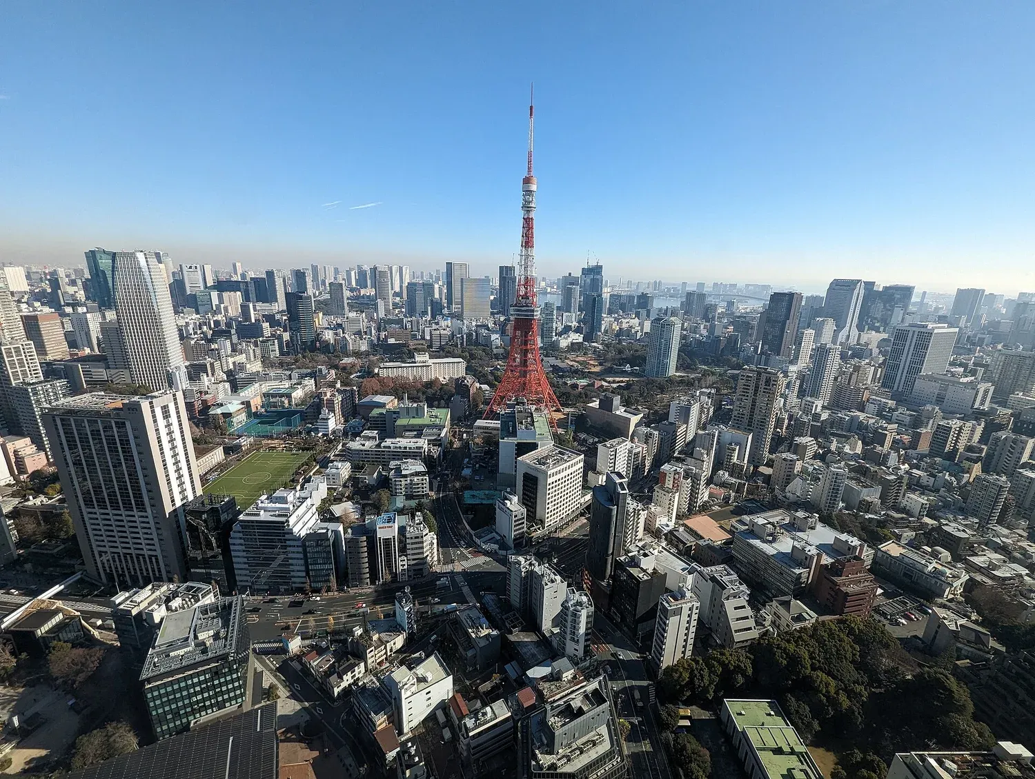 Tokyo Tower standing above a wide cityscape of Minato City, with Tokyo Bay on the horizon, seen from the 33rd floor of Azabudai Hills