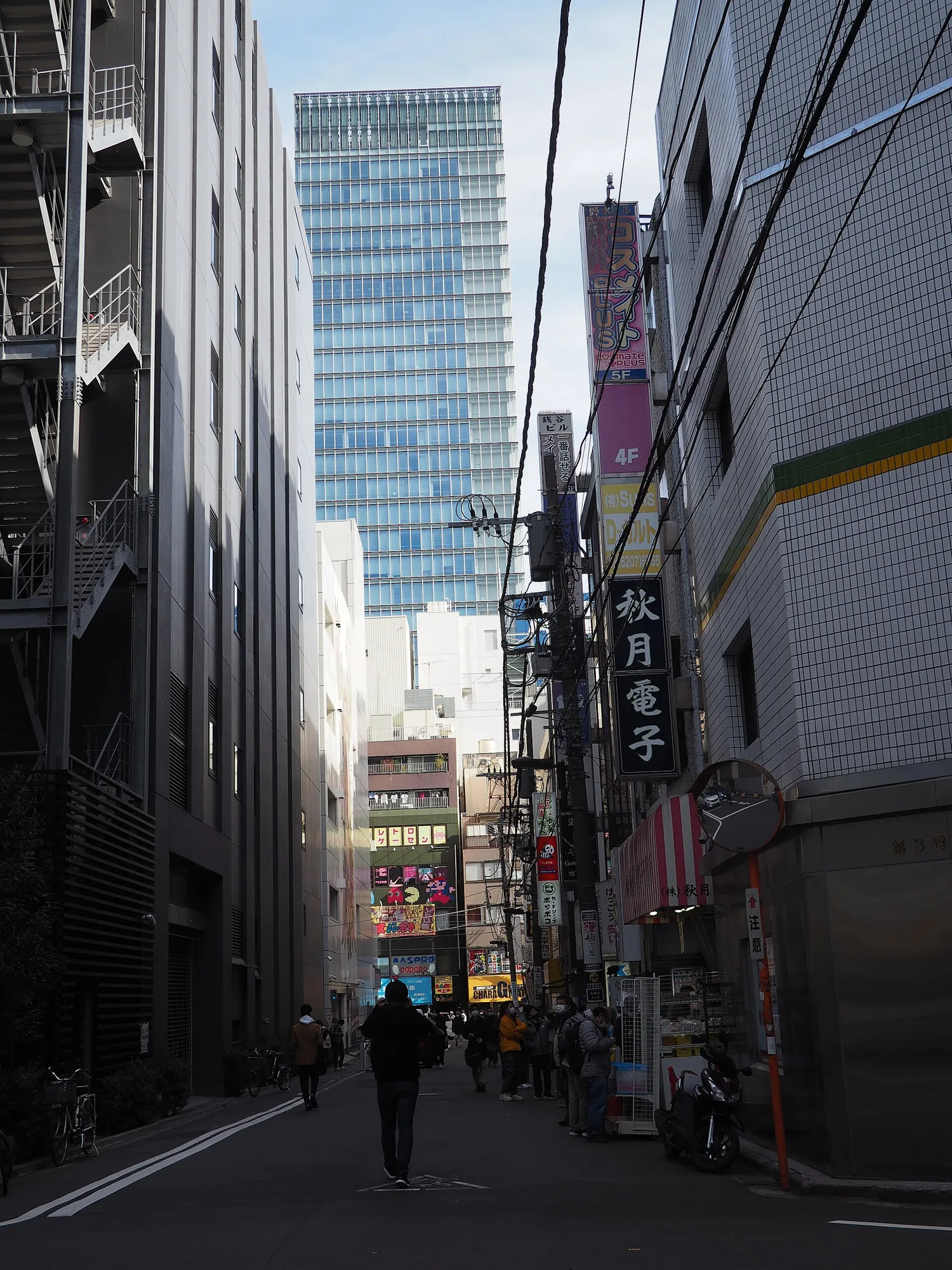 A narrow back street of electronic parts shops in Sotokanda 1-chome, Akihabara, with a vertical Akizuki Denshi sign and a high-rise behind