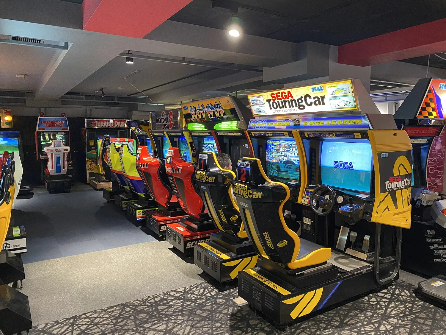 A row of old SEGA racing arcade cabinets with seats on the retro games floor of a GiGO building in Akihabara