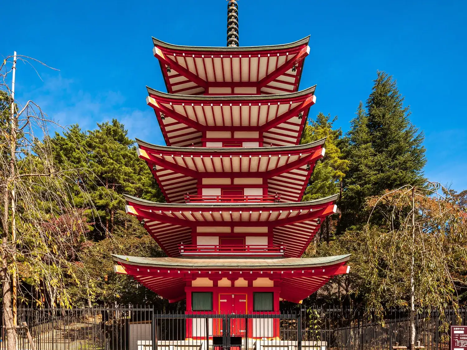 The vermilion five-storey Chureito tower among trees under a blue sky