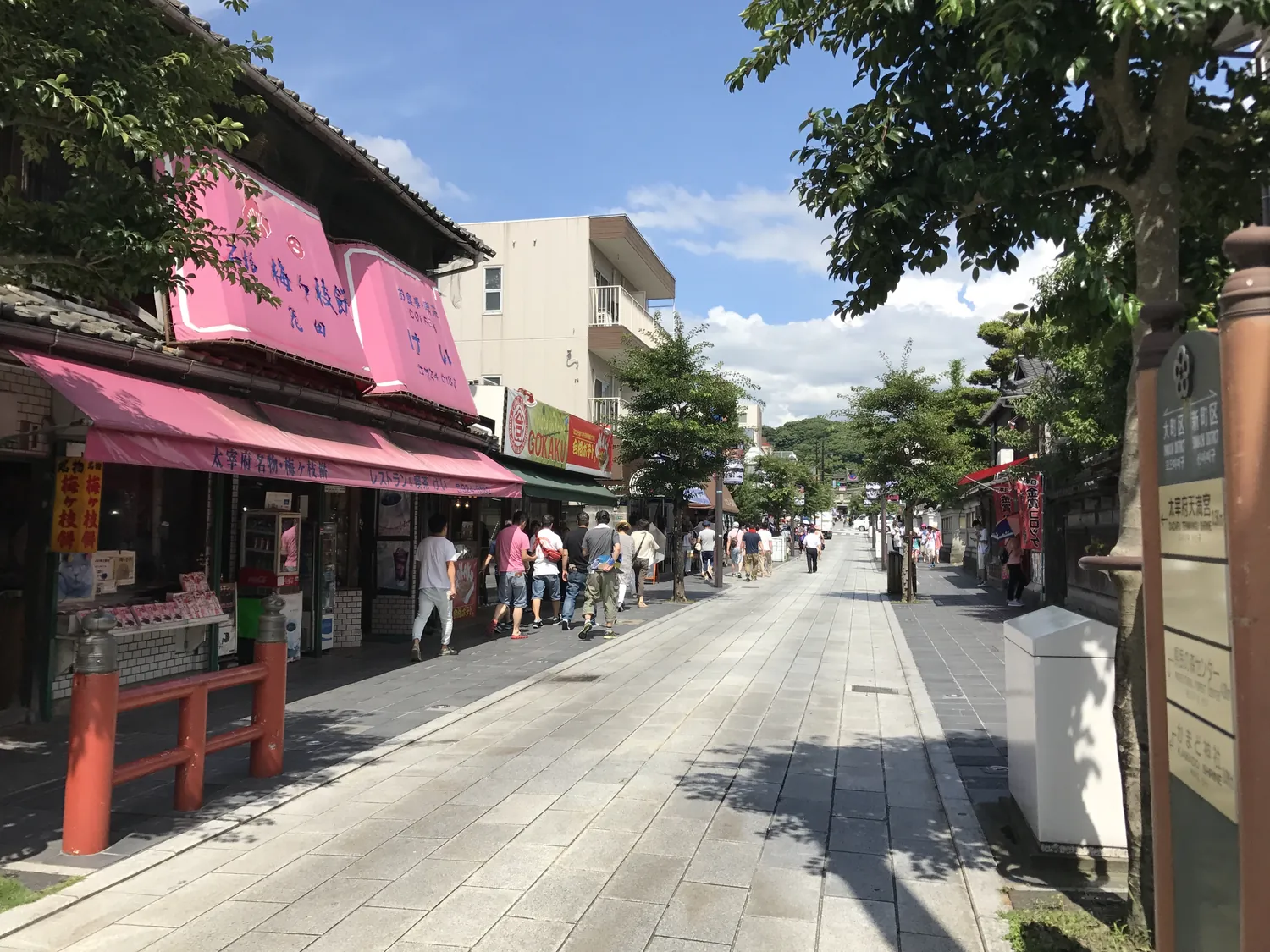 A street of low shops with a pink awning, leading toward trees