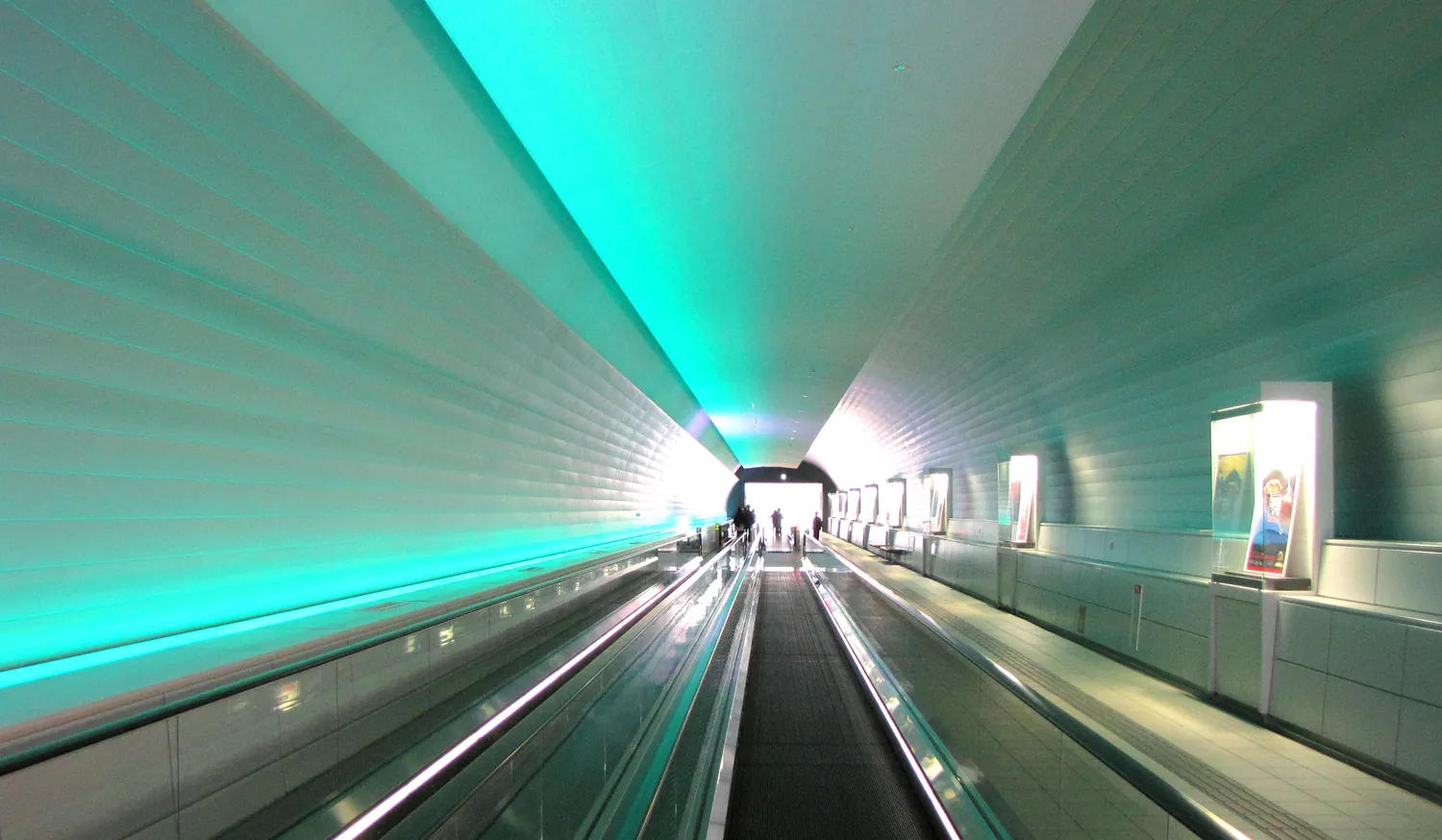 A long moving walkway inside a curved tunnel washed in green light