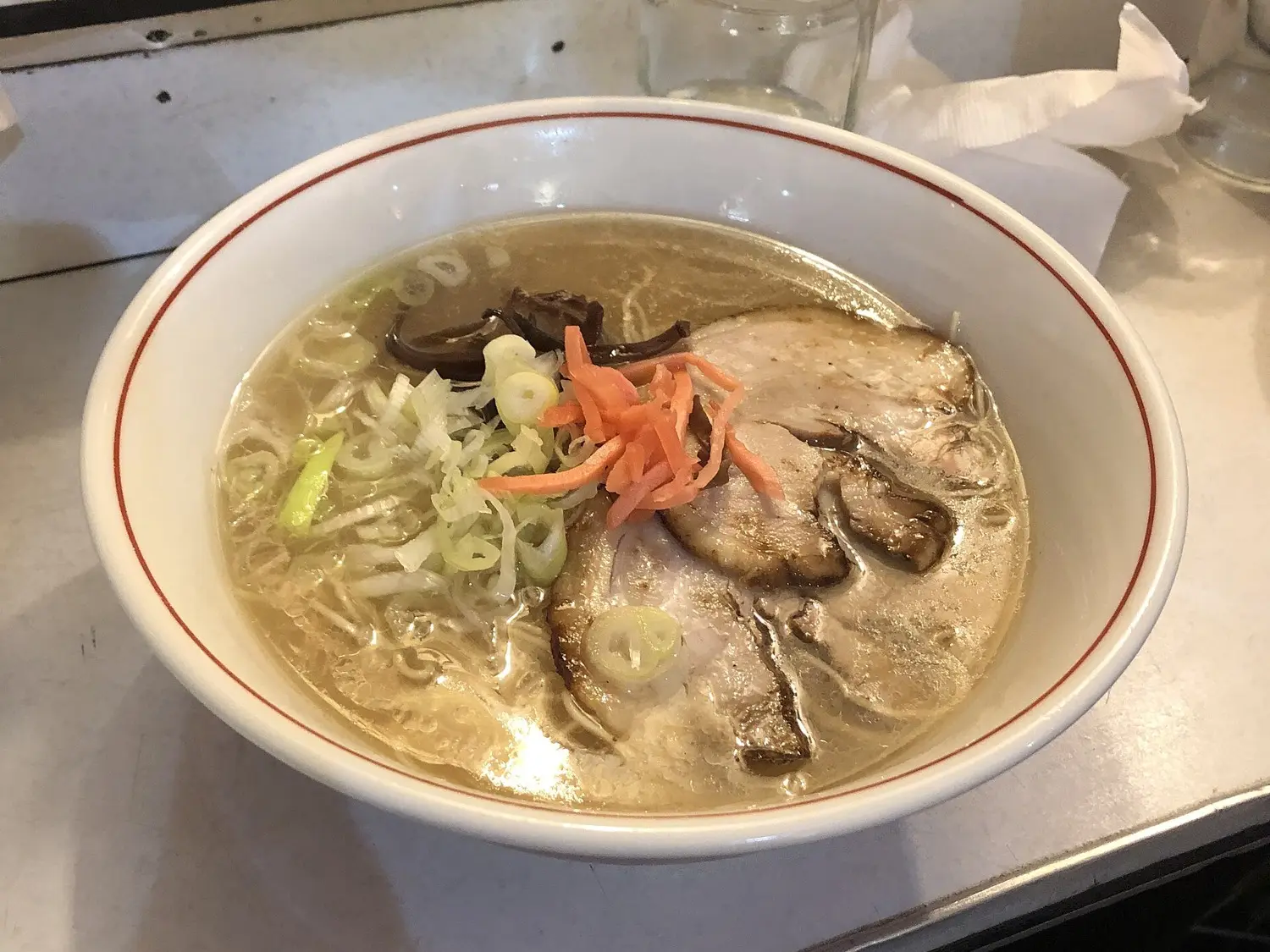 A bowl of Hakata ramen in cloudy pork-bone broth, topped with chashu pork, green onion, wood ear mushroom and red pickled ginger