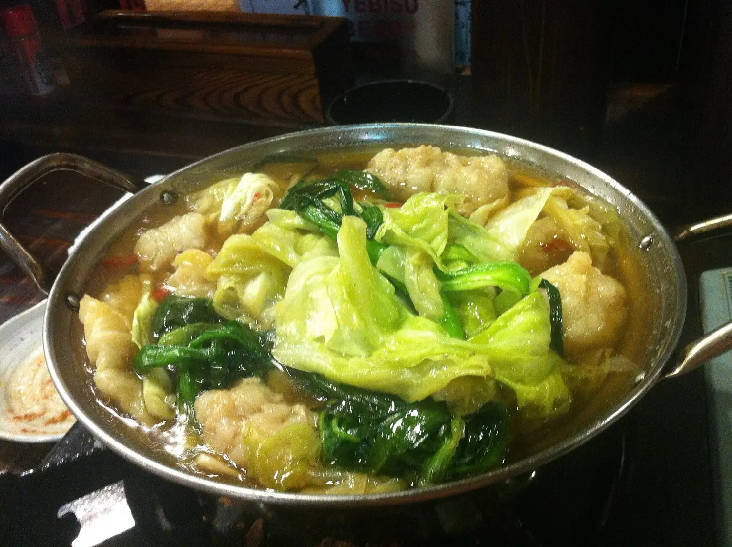 A metal pot of motsu nabe with cabbage, greens and pieces of offal in a light broth