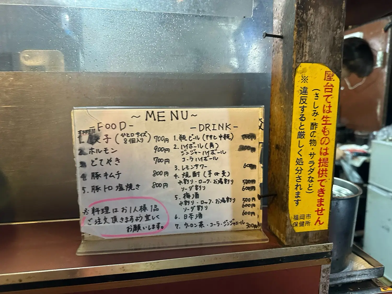 A handwritten menu board at a yatai, listing gyoza, offal and drinks with prices, and a note circled in pink