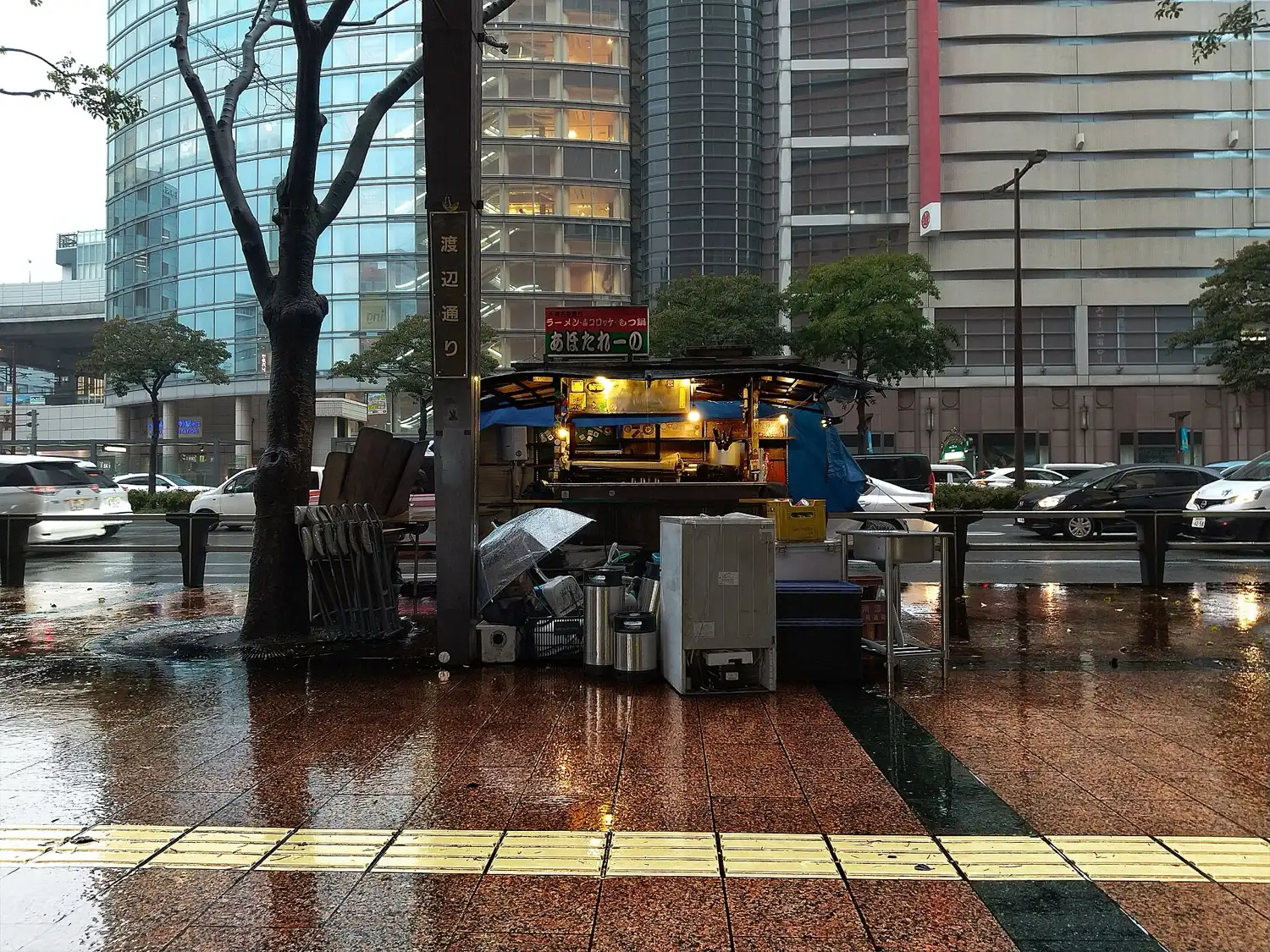 A yatai cart on a rain-wet sidewalk in Tenjin, with crates and equipment stacked beside it