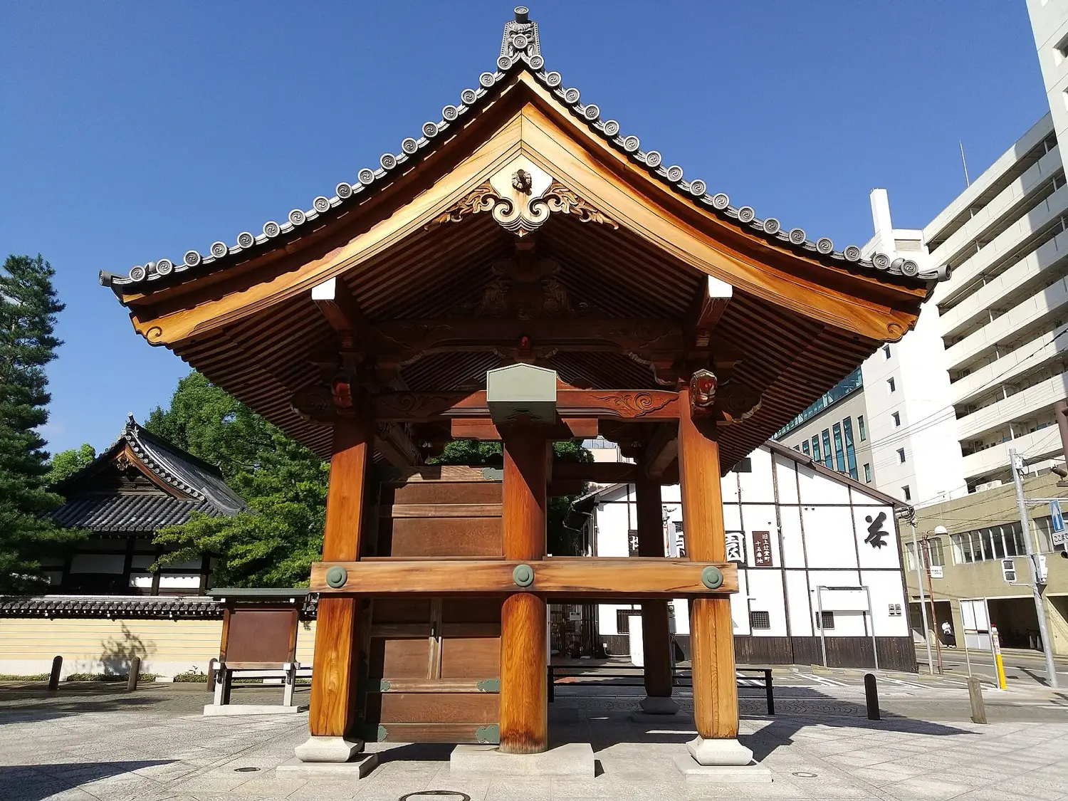 A wooden gate with a curved tiled roof standing on a paved street, with a white-walled building behind