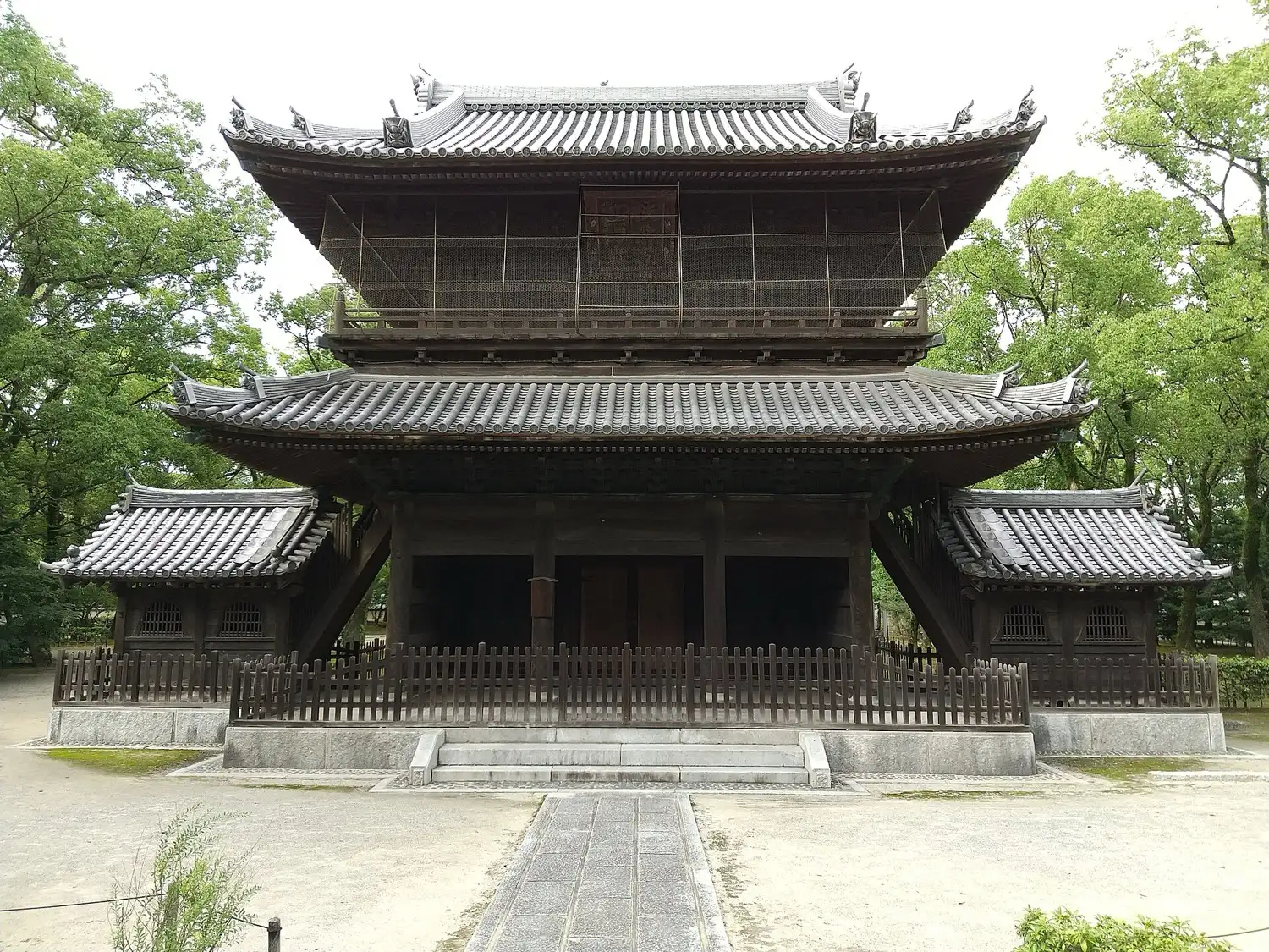 A large two-storied dark wooden temple gate with a stone path leading to it