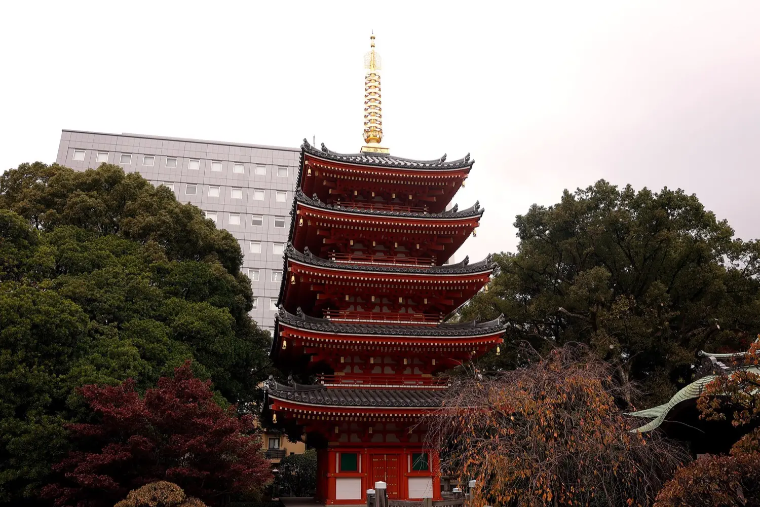 A red five-storied pagoda with a tall golden spire among trees