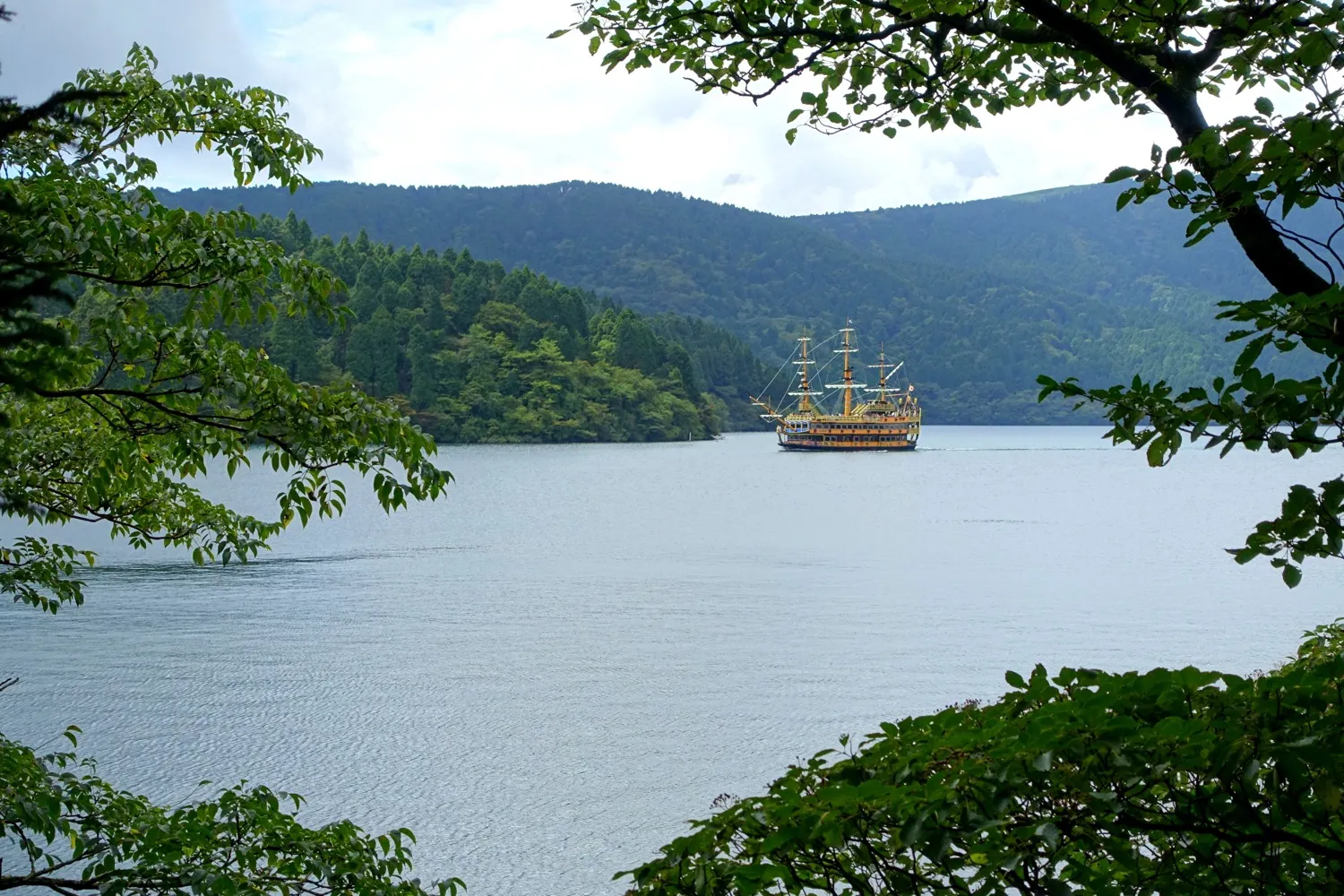Lake Ashi between forested hills, with a sightseeing ship on the water