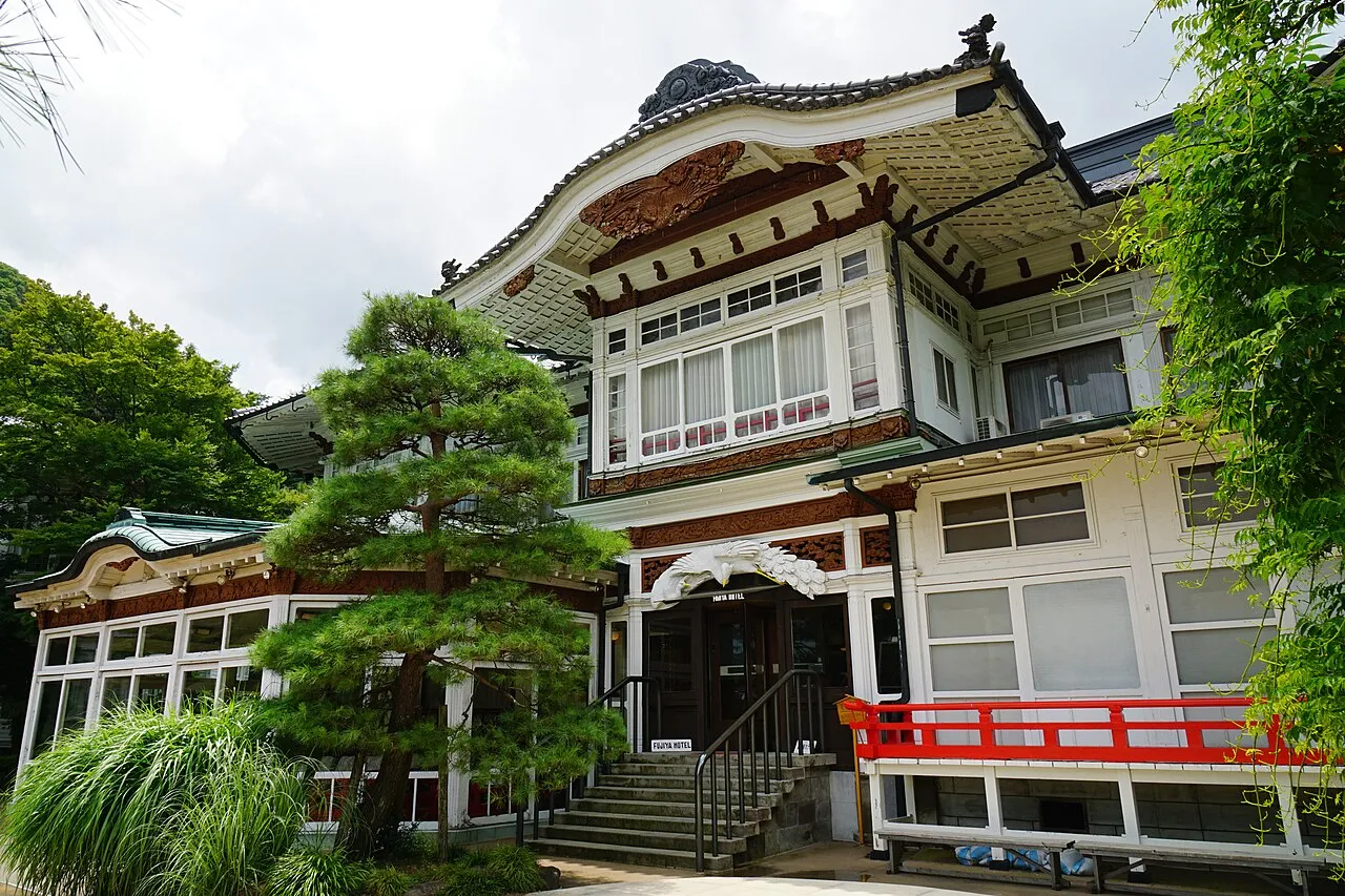 The Main Building of Fujiya Hotel, white walls under a tiled roof with a curved gable over the entrance, a red railing and a pine in front