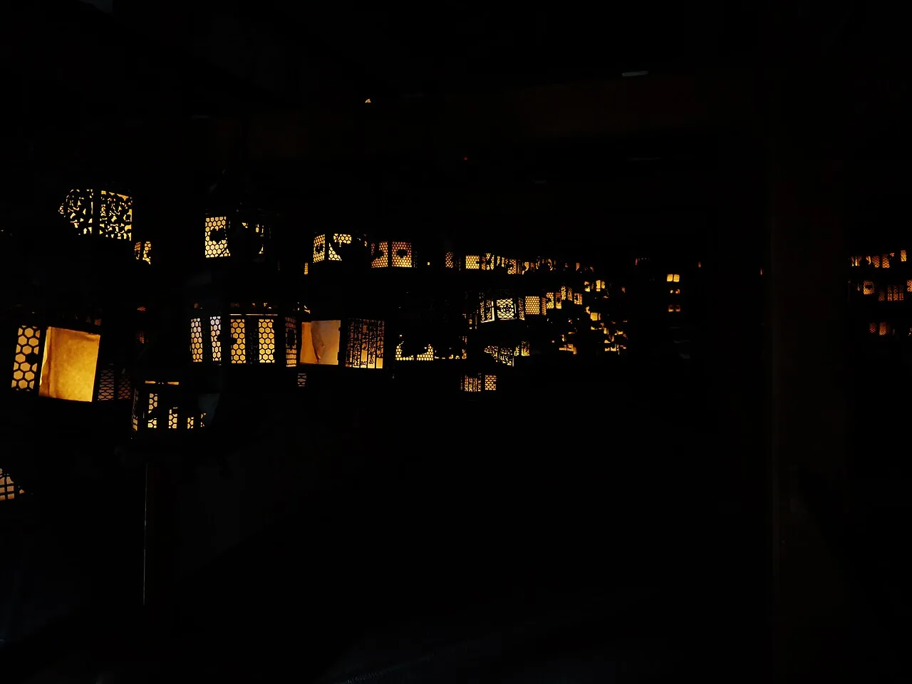 Rows of bronze hanging lanterns lit inside the dark interior of the Fujinami-no-ya at Kasuga Taisha
