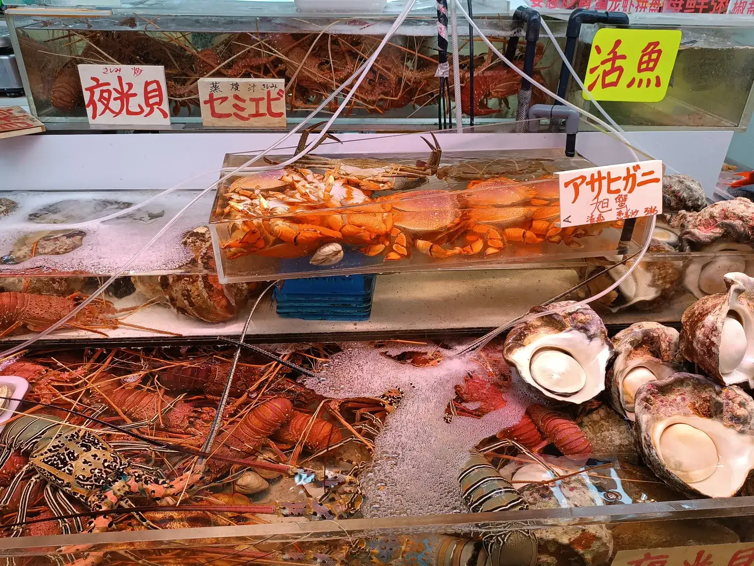 A seafood counter piled with spiny lobsters and large shellfish on ice, handwritten price cards above