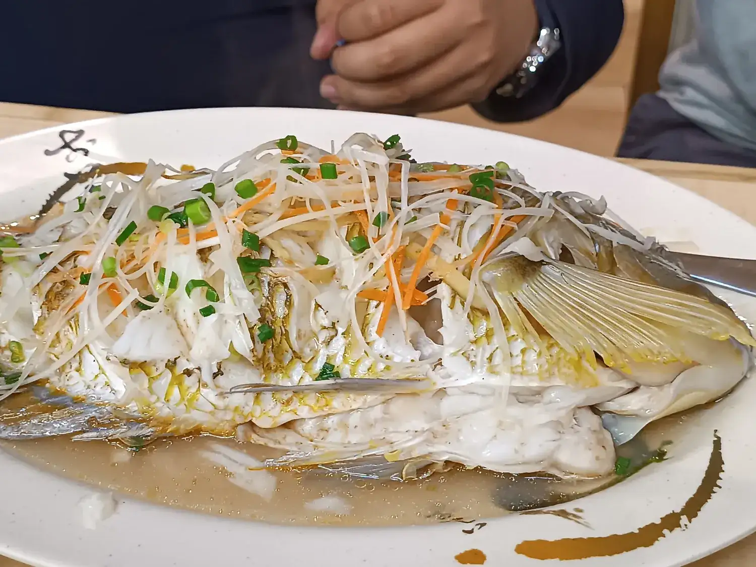 A whole steamed fish under shredded spring onion and vegetables on a white plate
