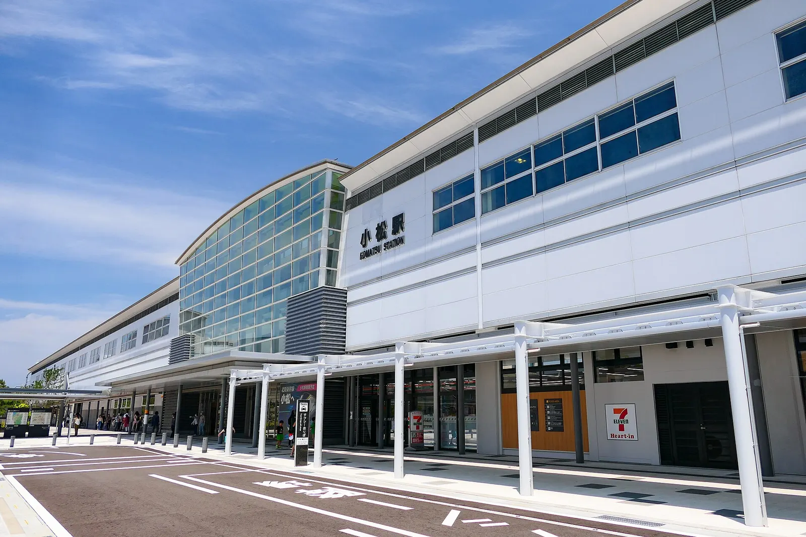 The long white station building of Komatsu Station seen from the west exit plaza under a blue sky