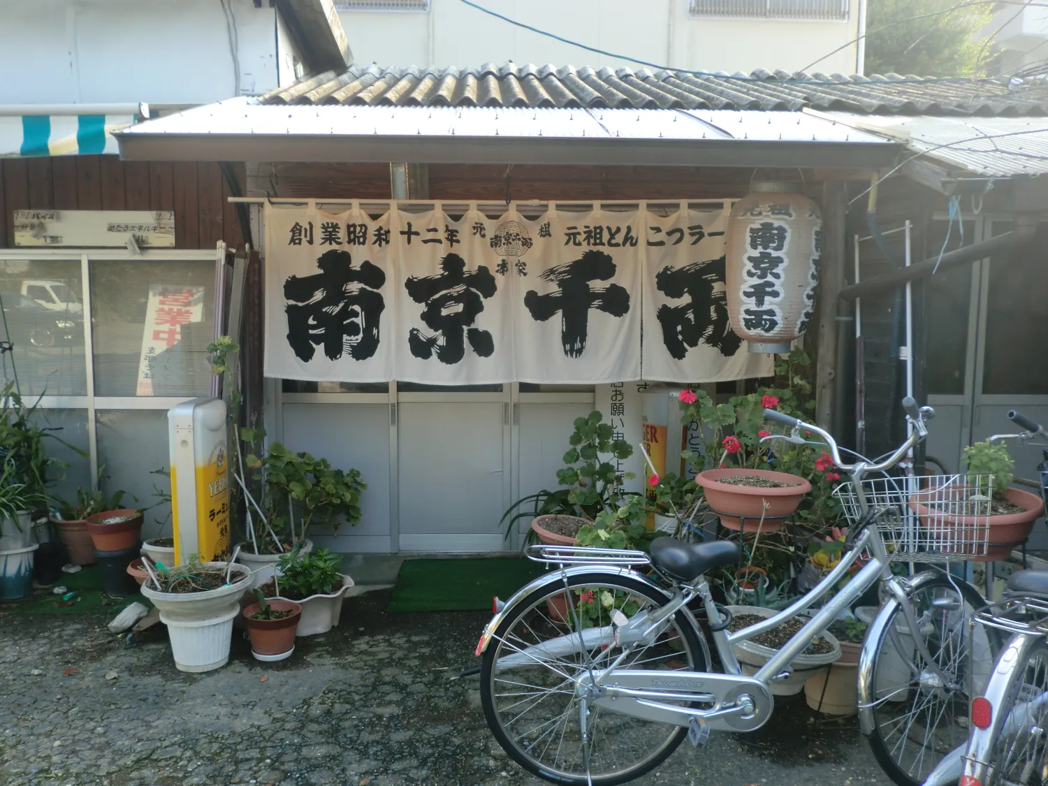 A small ramen shop front with a white curtain and signboard reading Nankin Senryo, with bicycles parked outside