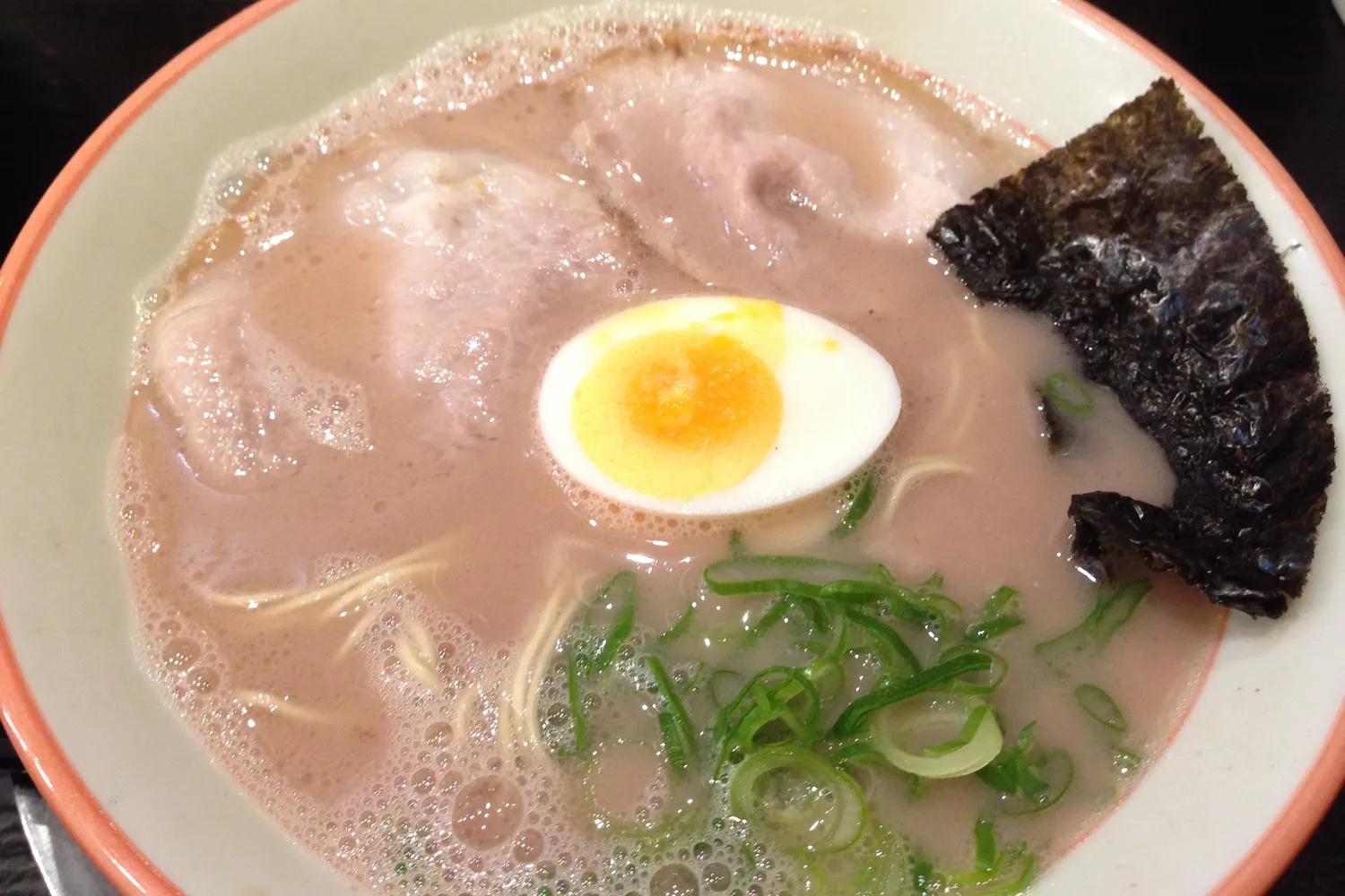 A bowl of pale, creamy pork-bone ramen with sliced pork, half a boiled egg, green onion and a sheet of seaweed