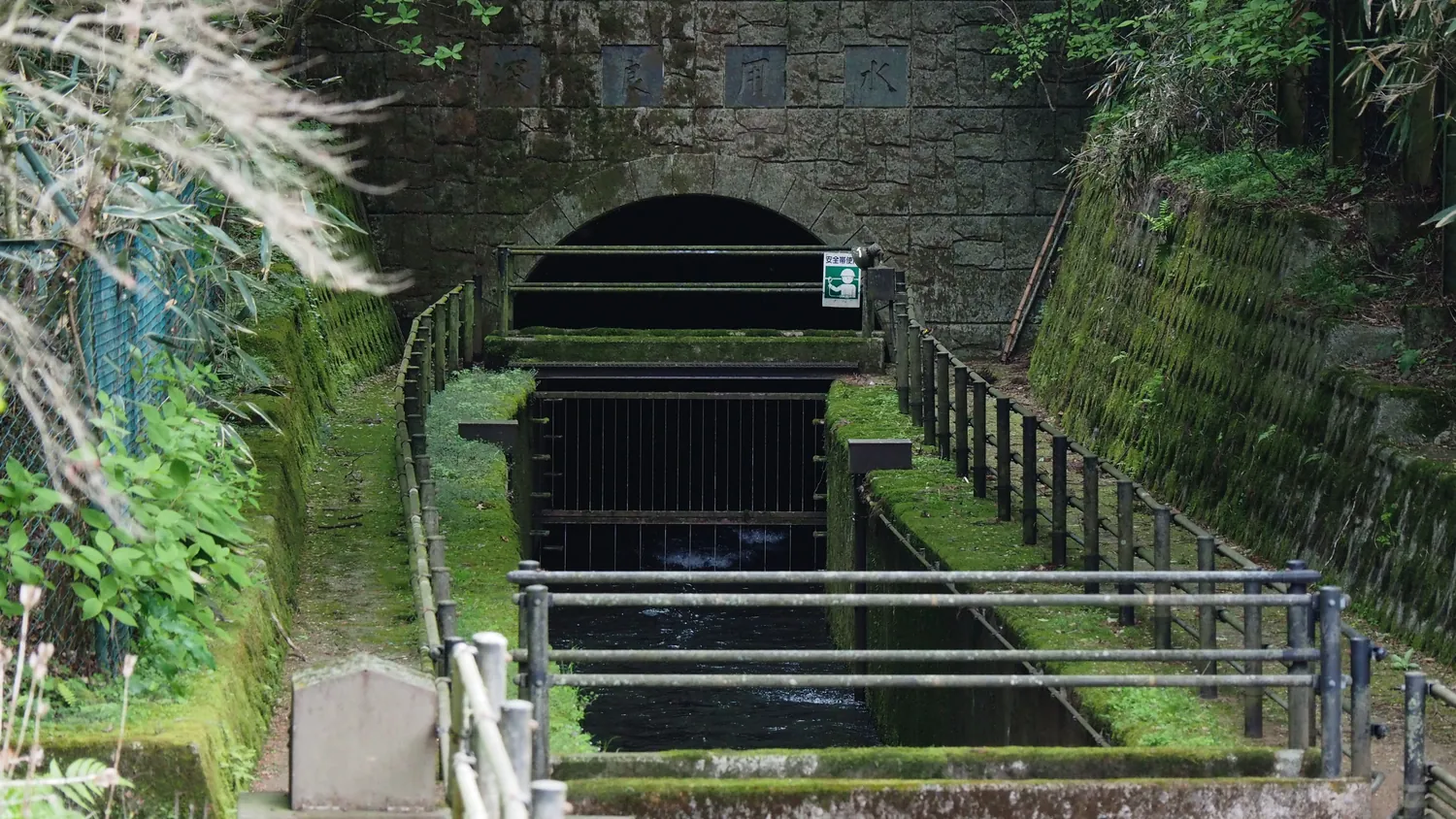 A stone-lined tunnel mouth with a channel of water, set in a green hillside