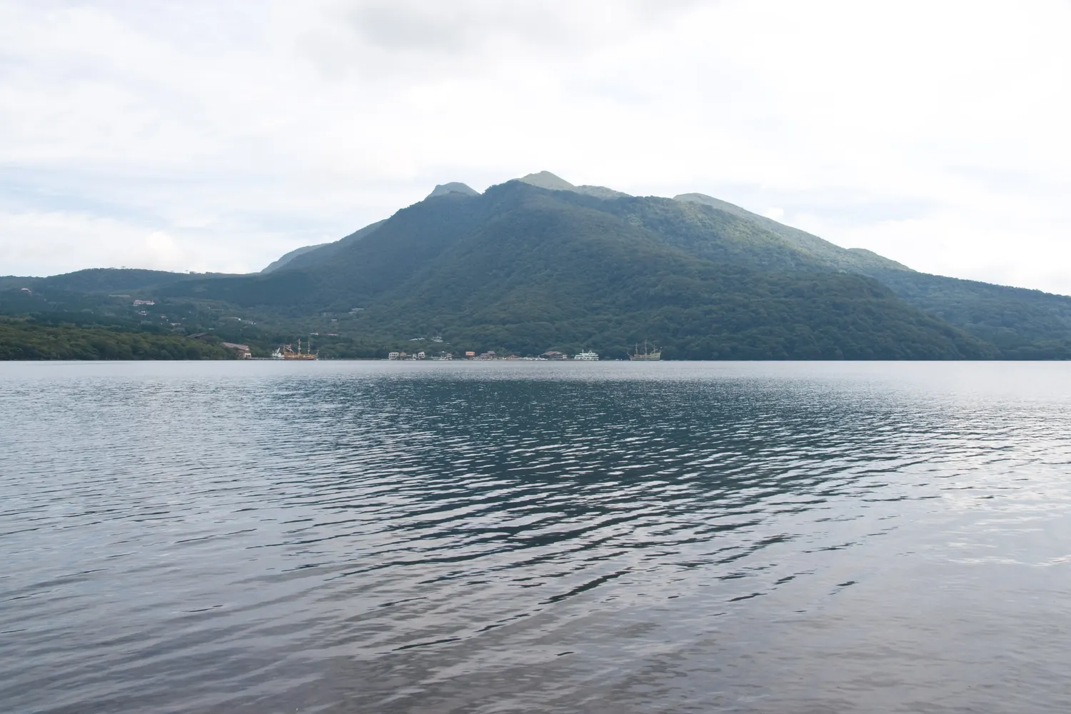 A dark, rounded volcanic peak rising behind the calm water of a lake