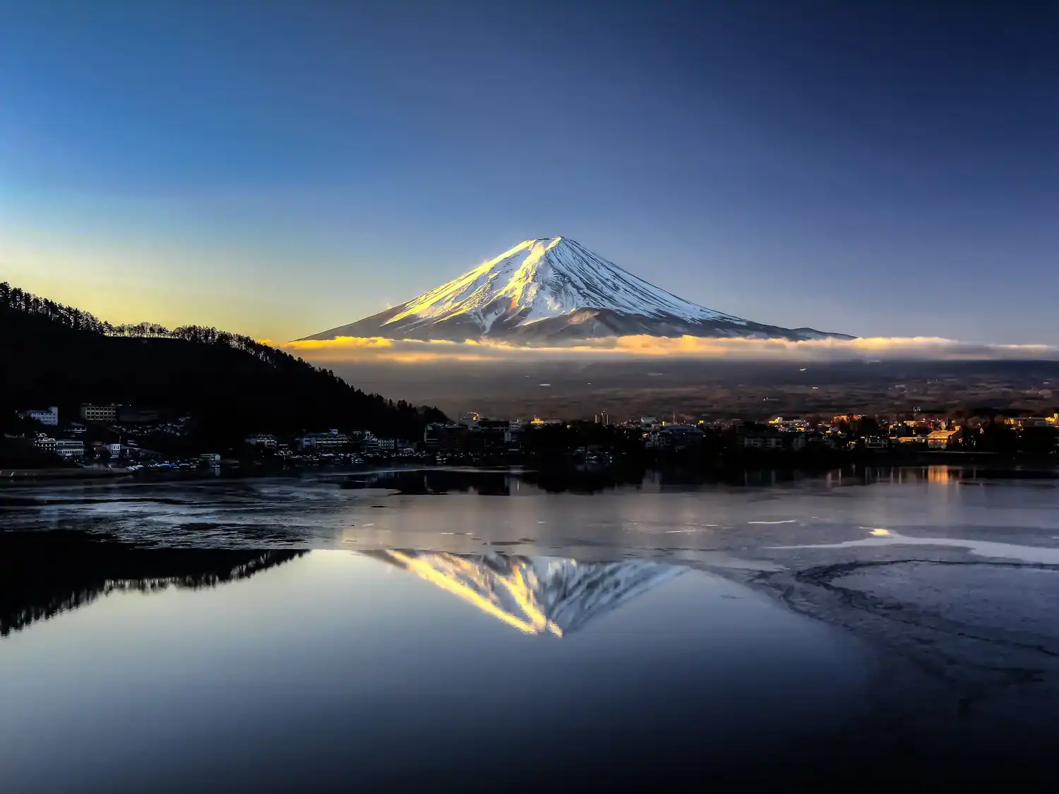 Mount Fuji at dawn across a calm Lake Kawaguchi, its snowy peak reflected in the water