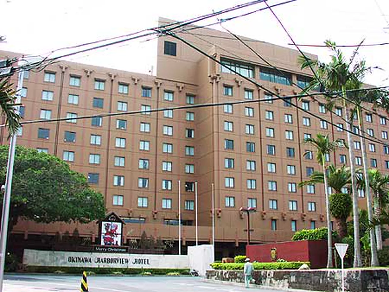 The ochre-red block of the Okinawa Harborview Hotel behind palm trees and a low hedge