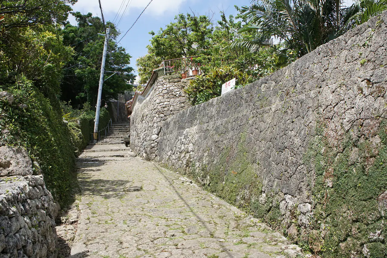 The Kinjo-cho stone path climbing between mossy limestone walls and green trees in Shuri