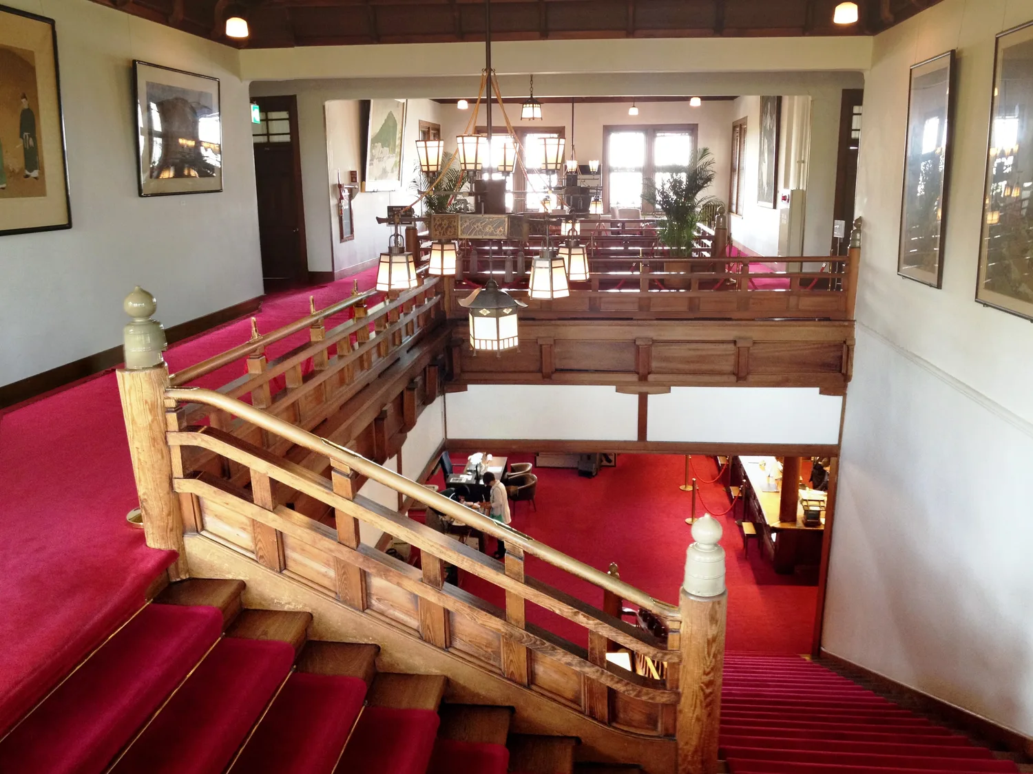 A red-carpeted wooden staircase seen from the landing above, leading down to a lobby hung with lanterns