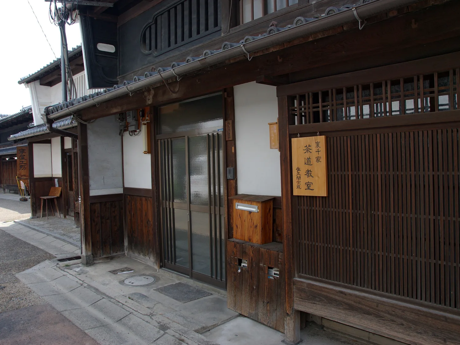 The dark wooden lattice front of an old townhouse on a narrow paved lane, a sign hanging by the door