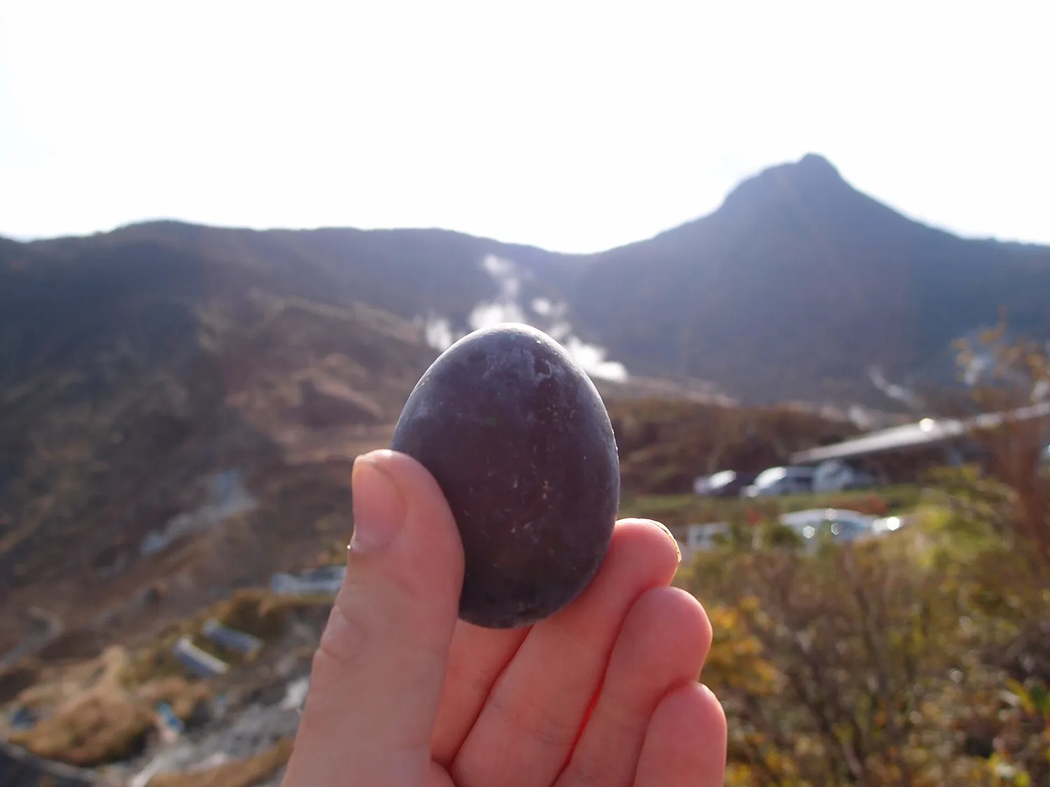 A black-shelled egg held up against the Owakudani slopes