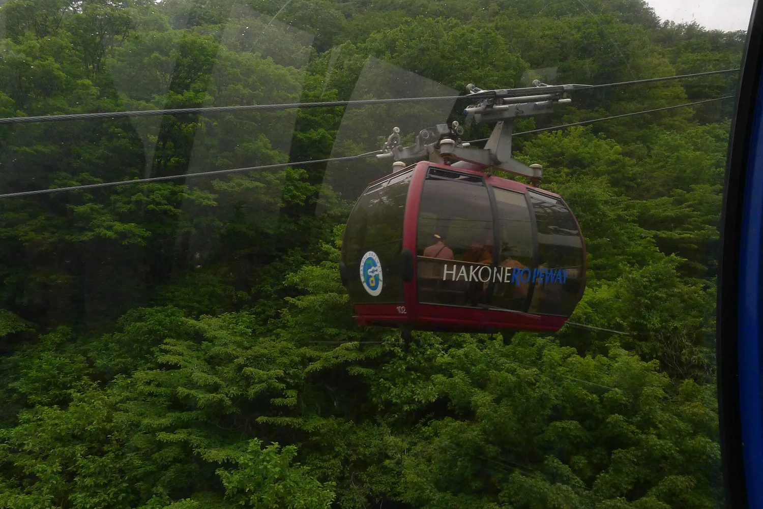 A red Hakone Ropeway gondola on its cable above a forested slope