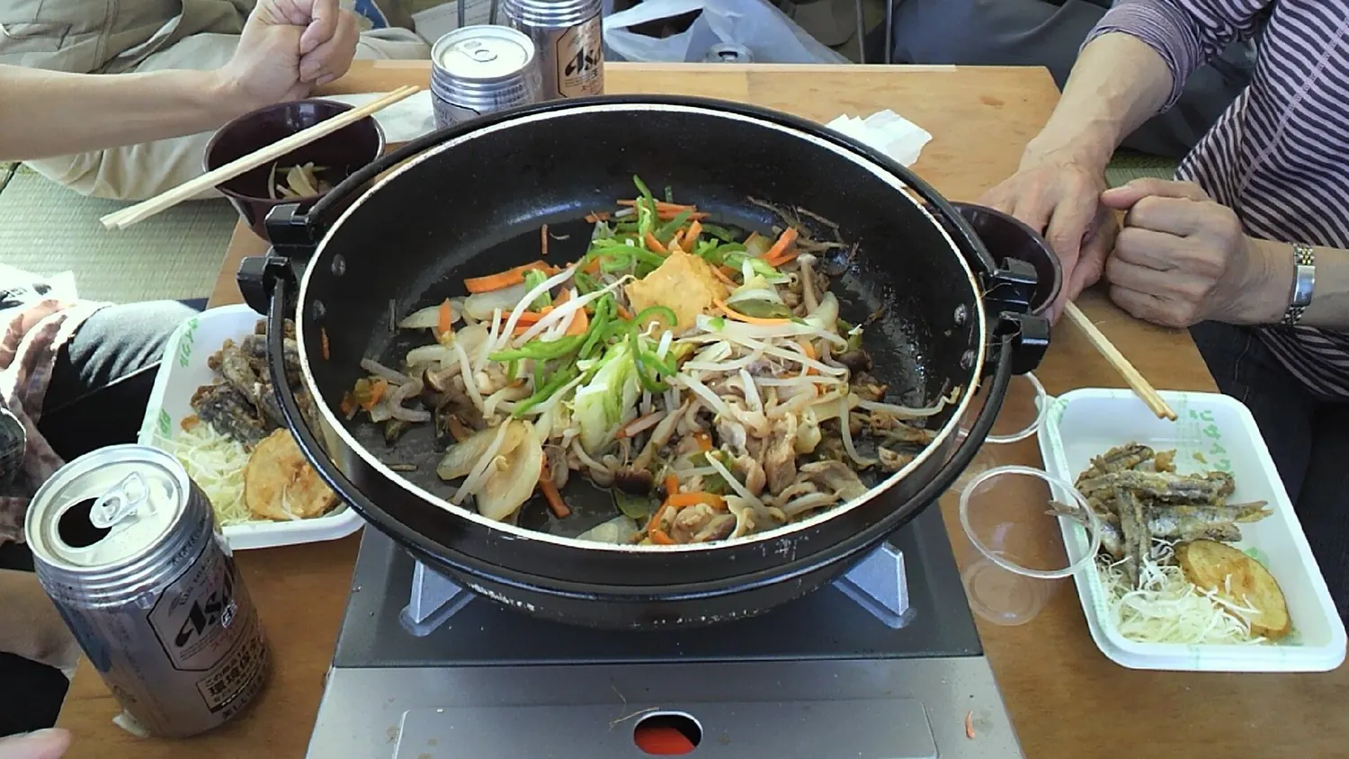A shallow pot of bishonabe with chicken, cabbage, leek and green pepper on a table beside small dishes