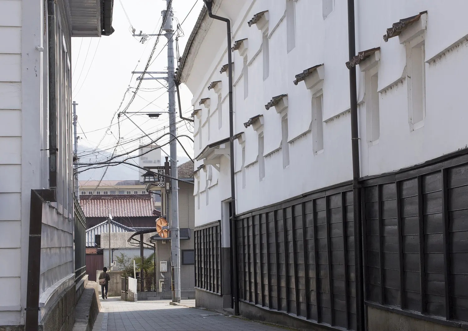 A narrow lane between white plaster sake storehouses with black lower walls