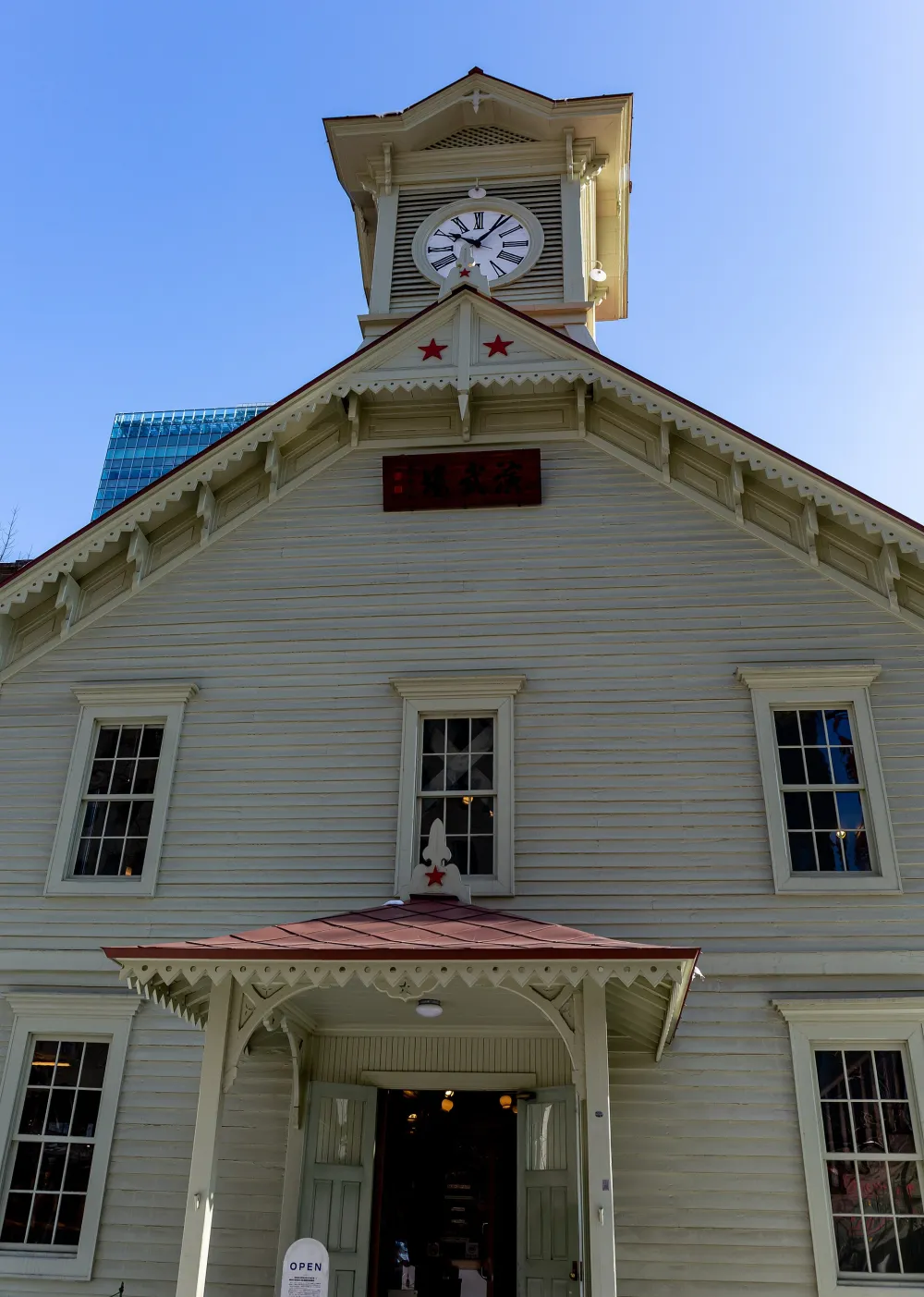 The white clapboard front of the Clock Tower seen from below, red stars on the gable and the clock face above