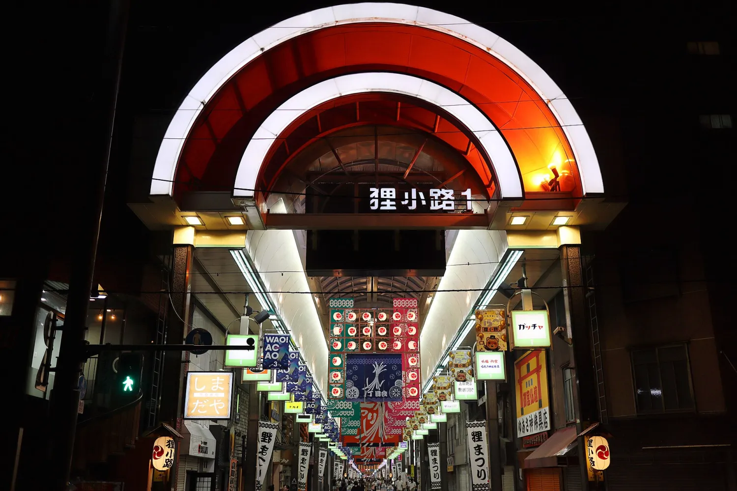 A lit arch at night over the entrance of a long covered shopping street, its sign reading Tanukikoji 1