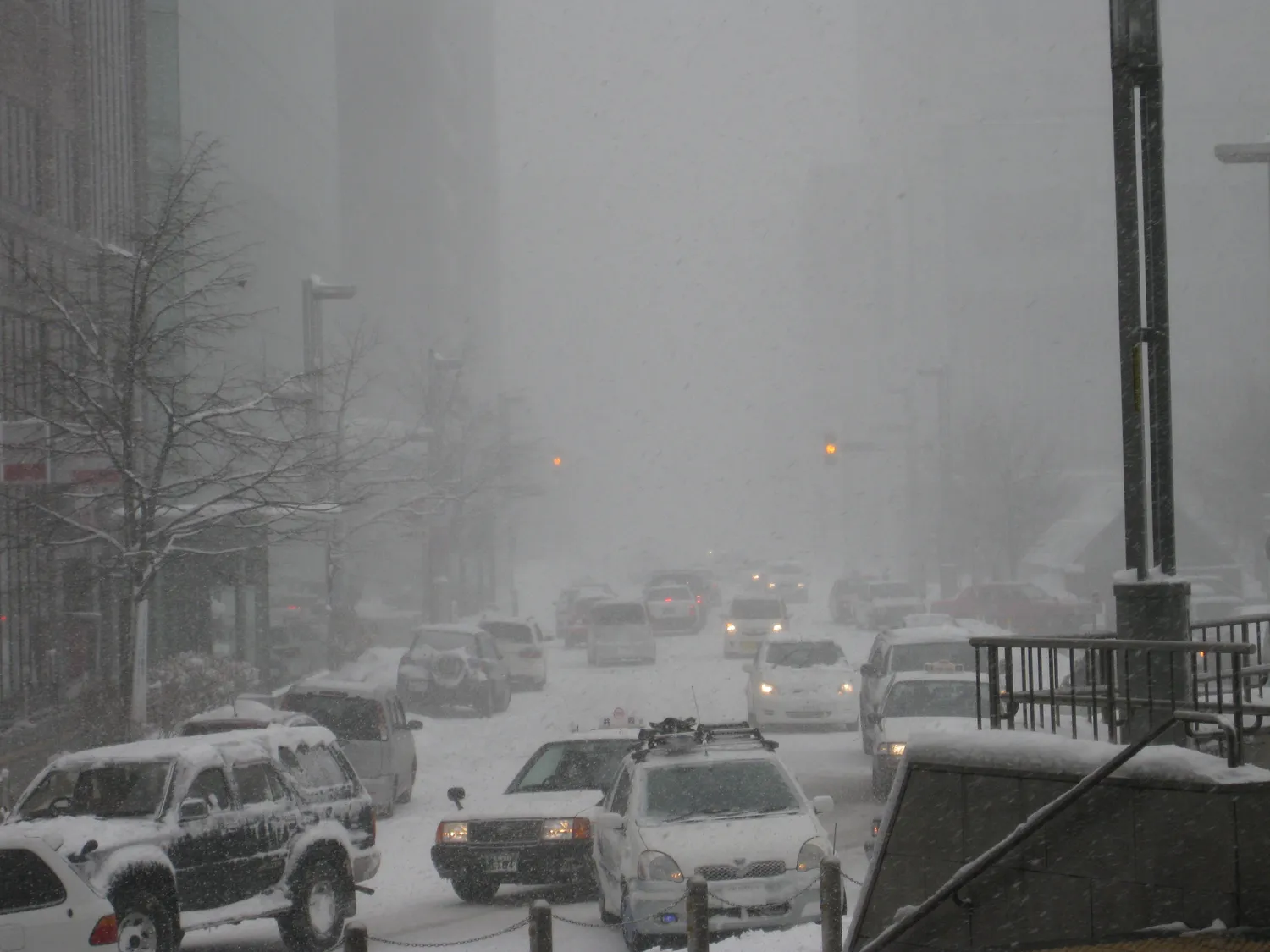 A Sapporo street in heavy snow, cars crawling through a white haze