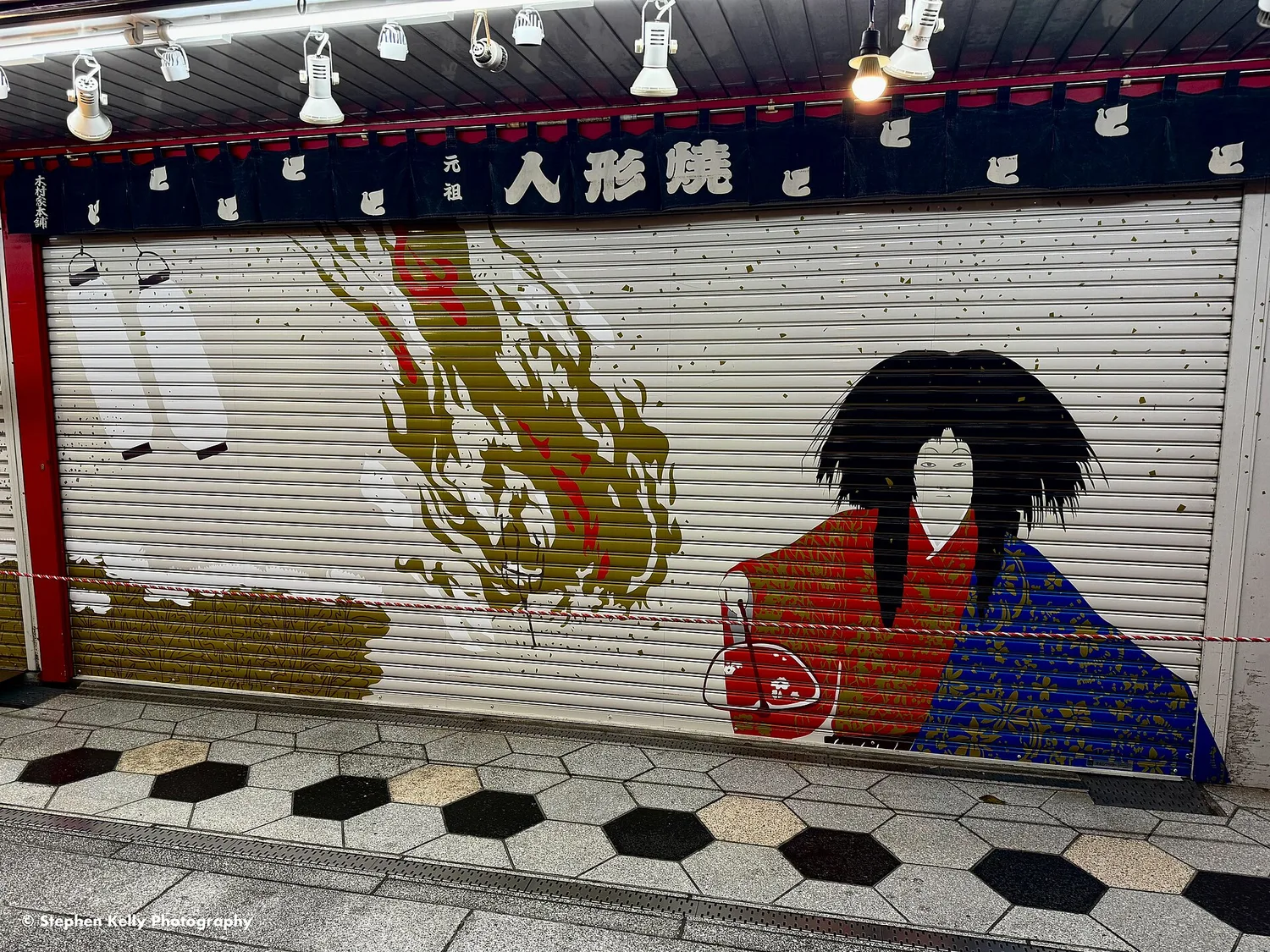 A closed storefront shutter on Nakamise shopping street painted with a figure in traditional costume and flames, seen at night