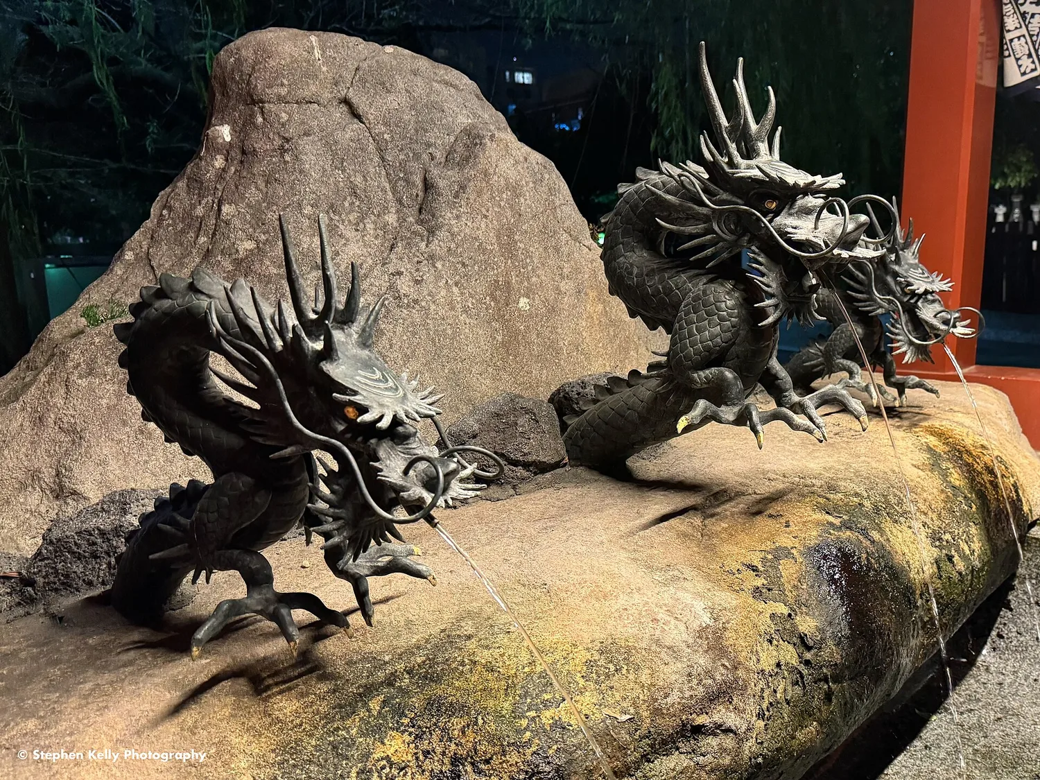 Bronze dragon sculptures coiled on a mossy rock at the purification fountain of Senso-ji, lit at night