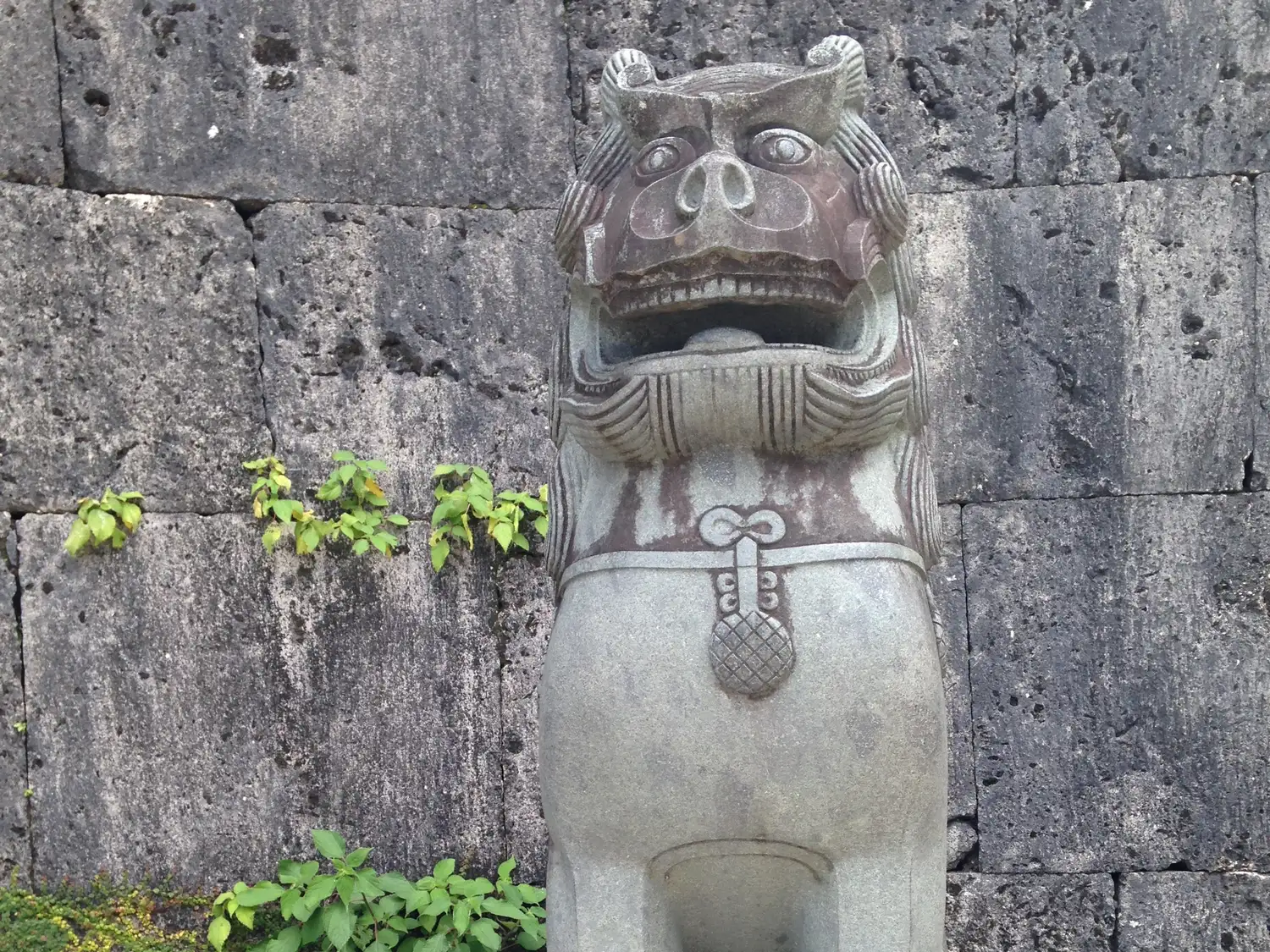A stone shisa lion standing against a wall of large limestone blocks