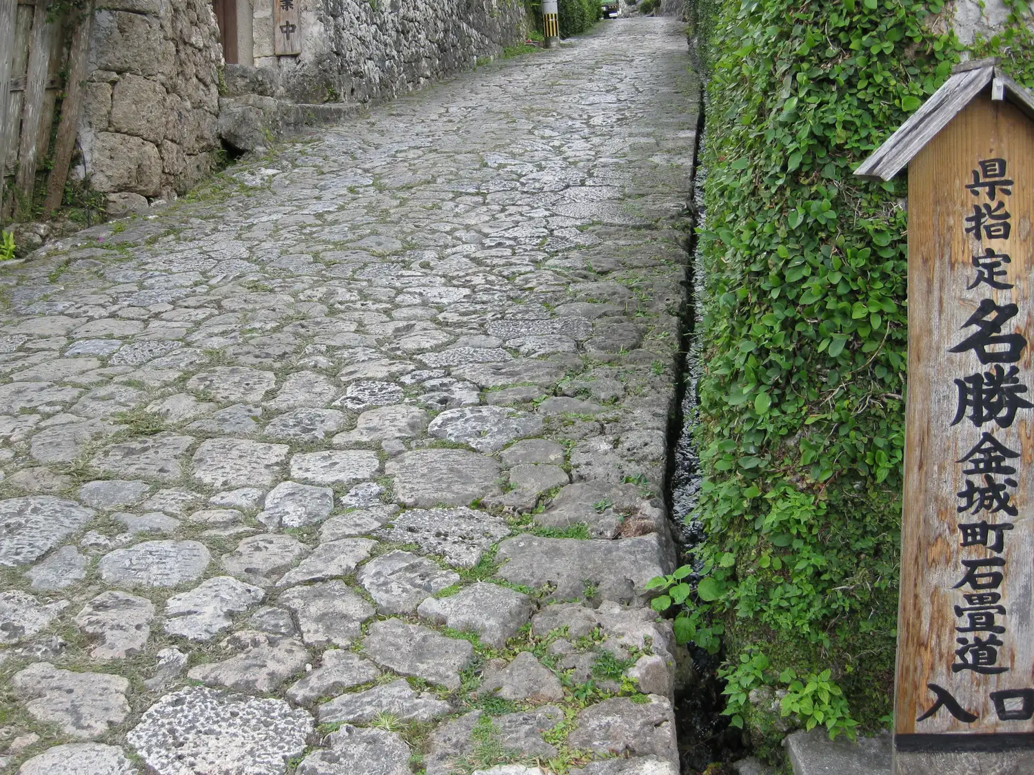 Irregular limestone paving climbing a narrow slope beside a stone wall, a wooden sign at the side