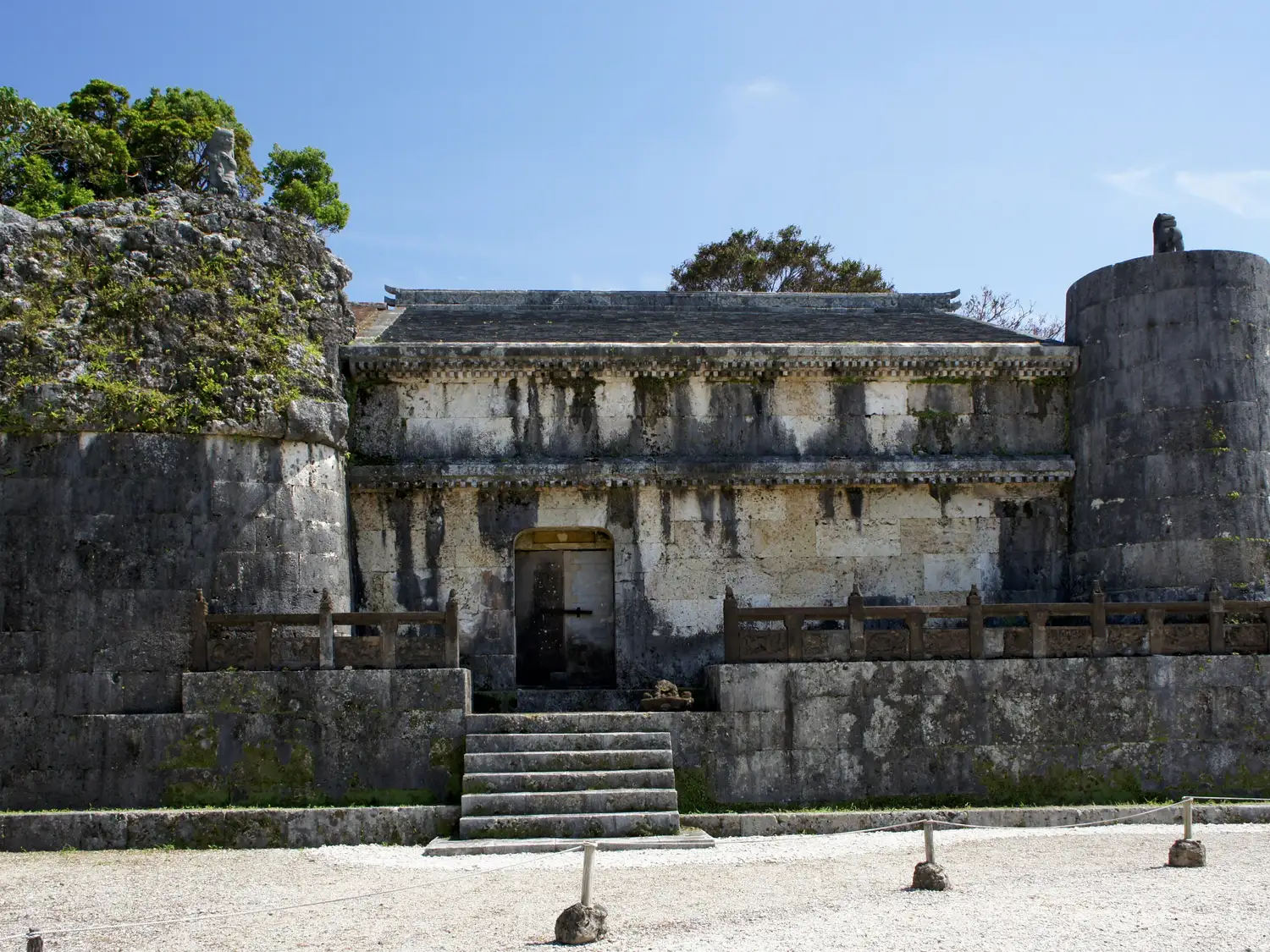 The stone front of a Tamaudun tomb chamber with steps, set behind a stone wall under a blue sky